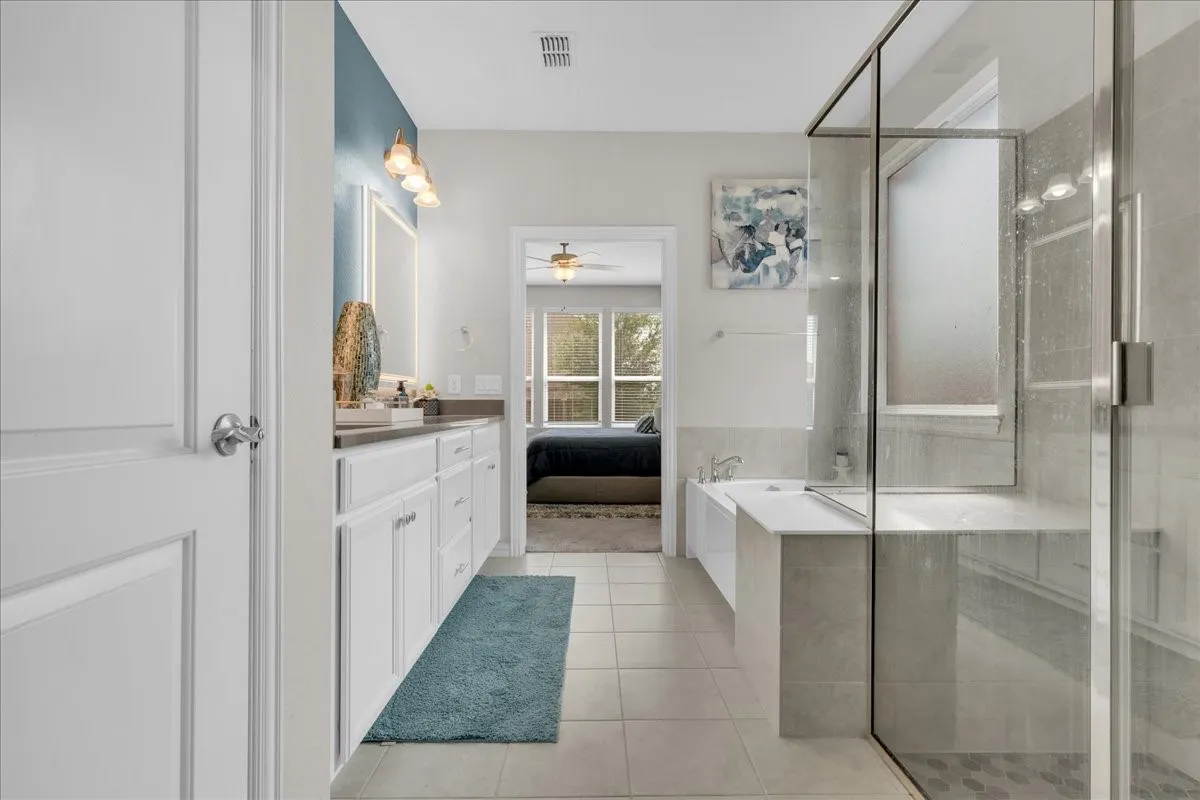 Contemporary bathroom featuring a spacious glass-enclosed shower, a separate built-in bathtub, dual vanity sinks with white cabinetry, and light-colored tile flooring
