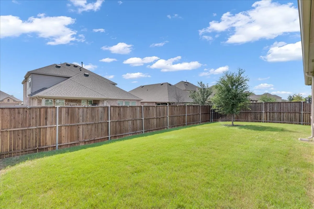 Expansive backyard featuring a lush lawn, a mature tree, and a full privacy fence