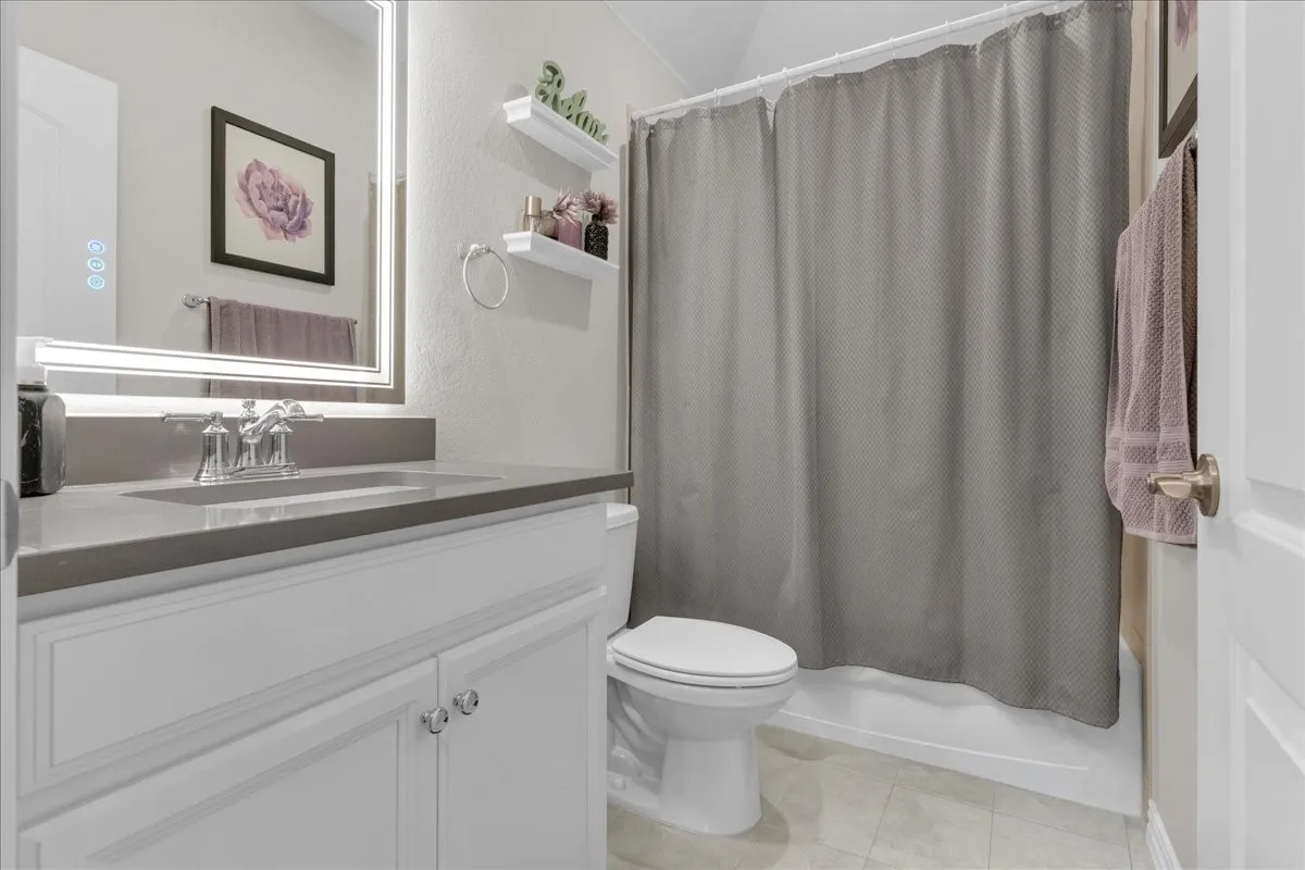 Bathroom featuring a white vanity with double-door cabinetry, grey countertop with an integrated sink, polished chrome faucet, and an illuminated mirror