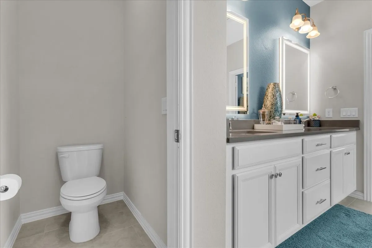 Dual vanity with white cabinetry, a stone countertop, and two illuminated mirrors