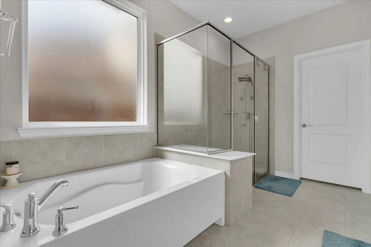 Bathroom featuring a large soaking tub with chrome fixtures, a frosted window, and a glass-enclosed shower with multiple showerheads