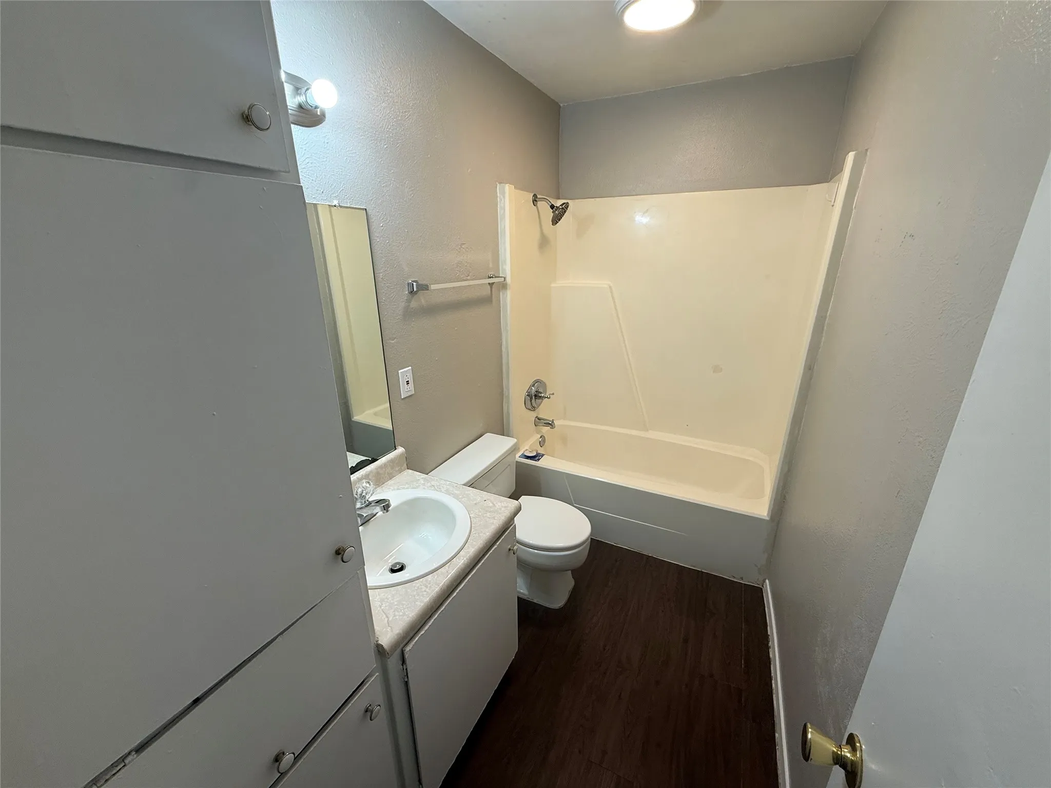 Bathroom featuring a single vanity with an integrated sink, a built-in medicine cabinet, a toilet, a tub/shower combination, and wood-finish flooring