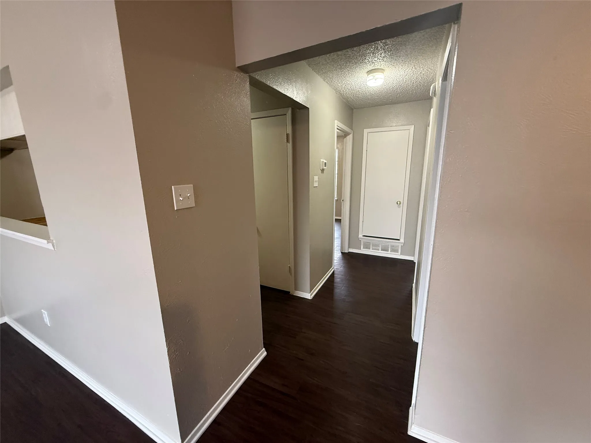 Hallway featuring dark wood-finish flooring, light neutral walls, and white trim