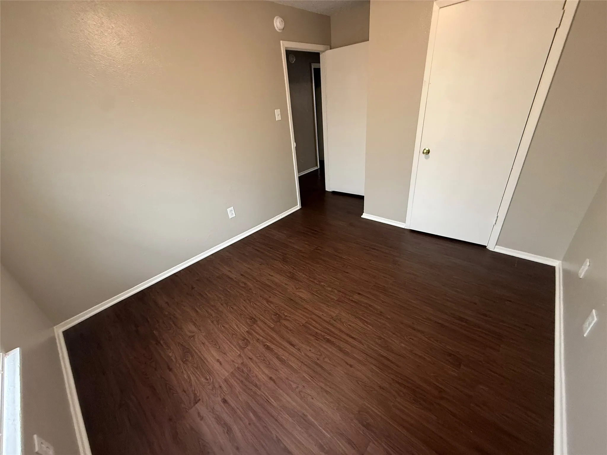 Spacious room featuring rich wood-finish flooring, light neutral-toned walls, and white baseboards