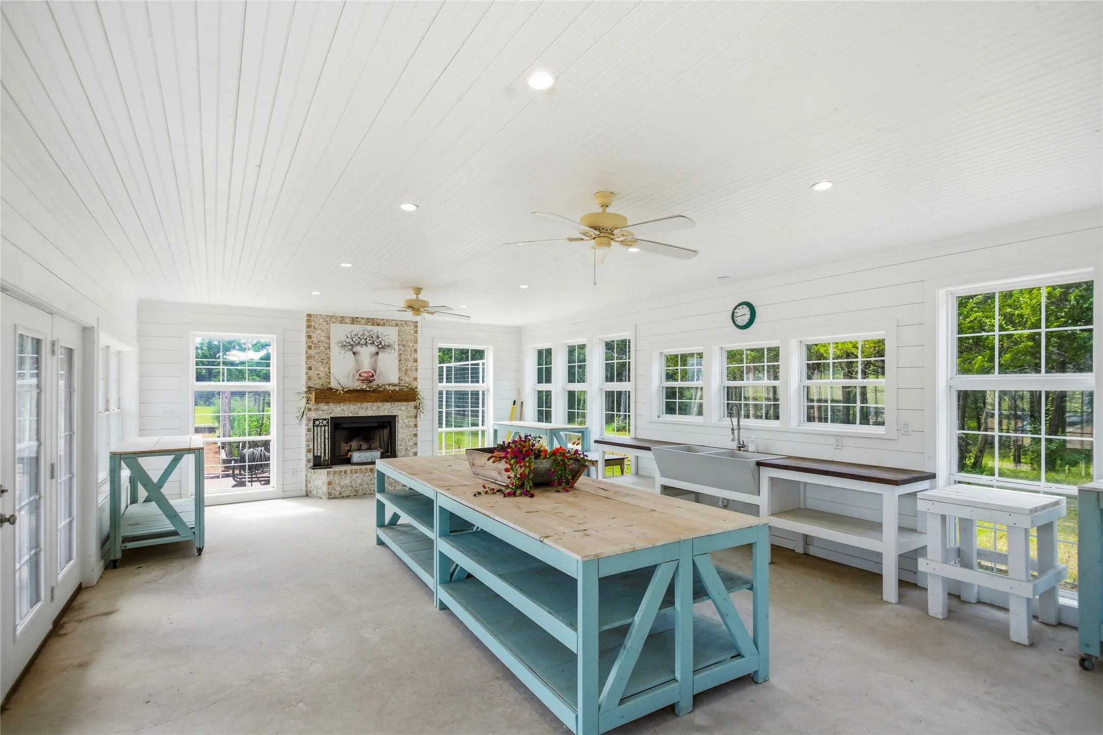 The main floor of the garden house has a wood burning fireplace, a farmhouse sink and garden tables - all in a room flooded with natural light through the abundance of windows.