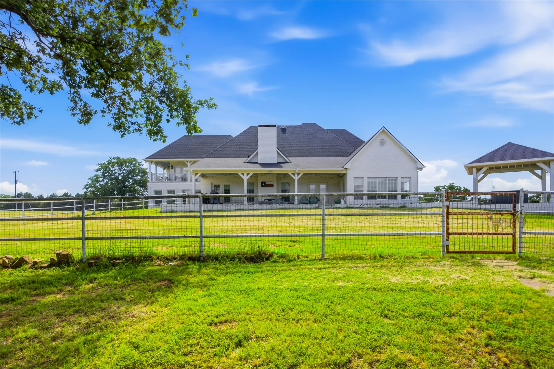 From the pond, you can get a view of the back of the home.  You can see the wrap around porch off upstairs bedroom 3, the large covered porch. and the Primary Bedroom sunroom that leads out to the porch.  The covered hot tub area is also pictured here.  There is a nice walkway out to it.