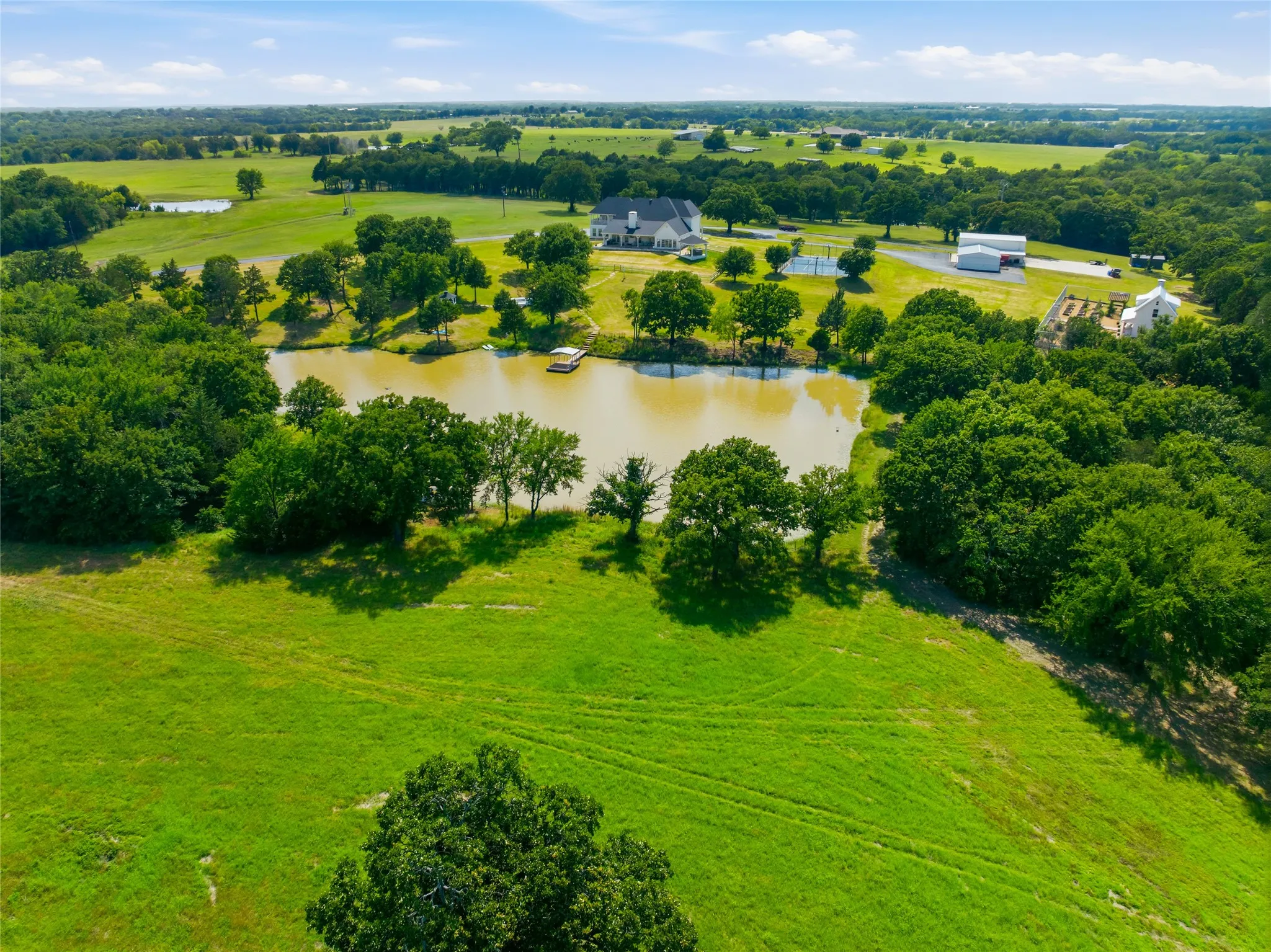 The back aerial view of the pond and property tells the story here - a beautiful house, ponds, rolling hills, am gorgeous trees, a green house and garden, a pickleball court and a double garage with 2 RV spaces and 2 garage spaces with plenty of shop space in between.