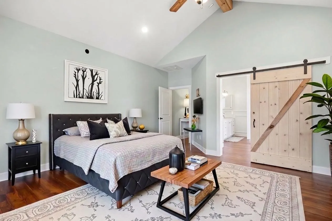 On the left side of the main entrance area, a vaulted ceiling draws your attention to this thoughtfully designed primary bedroom suite. The open barndoor leads to the primary bath area.