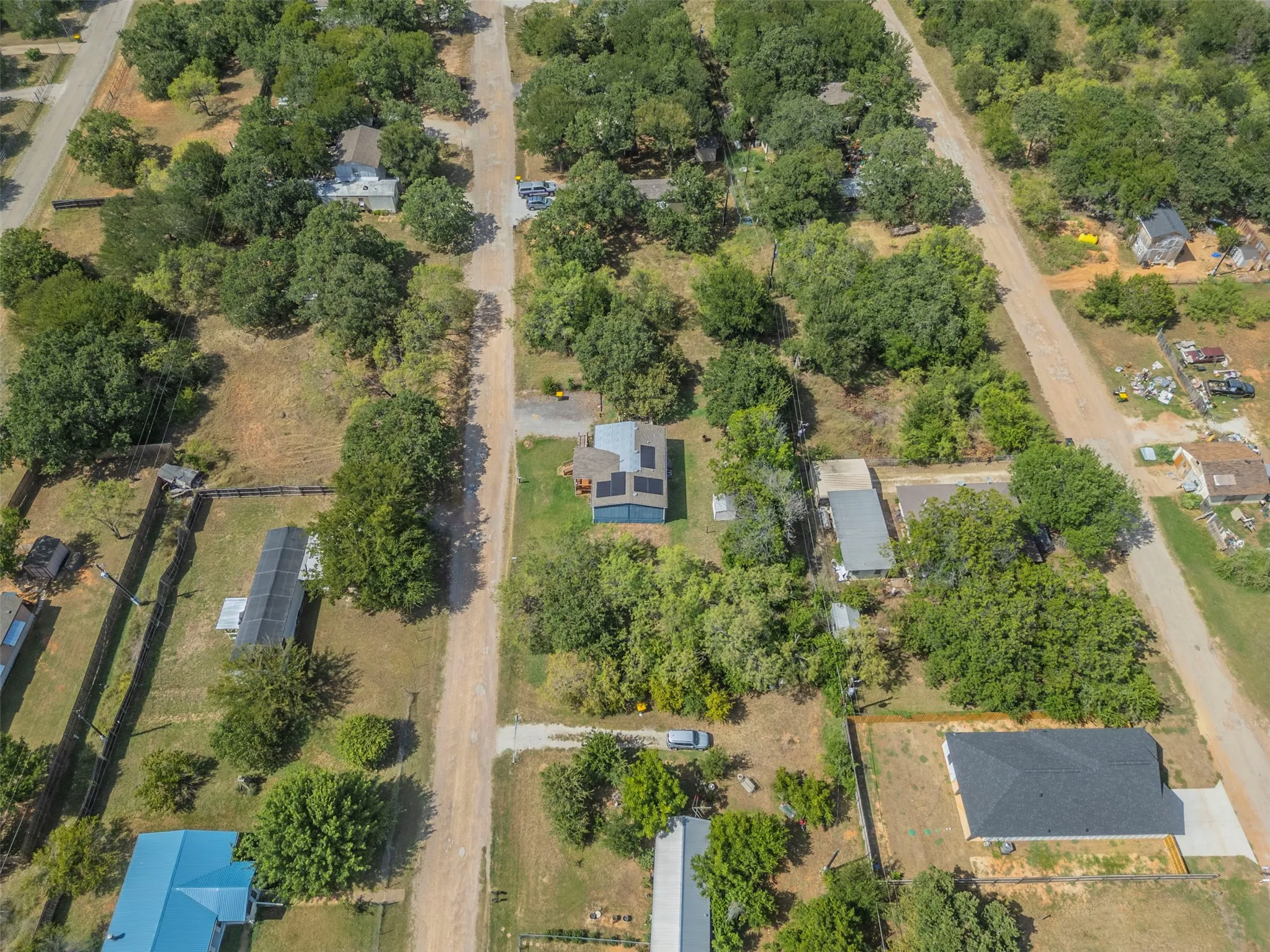 Aerial view of a residential property with surrounding mature trees, unpaved roads, and multiple structures