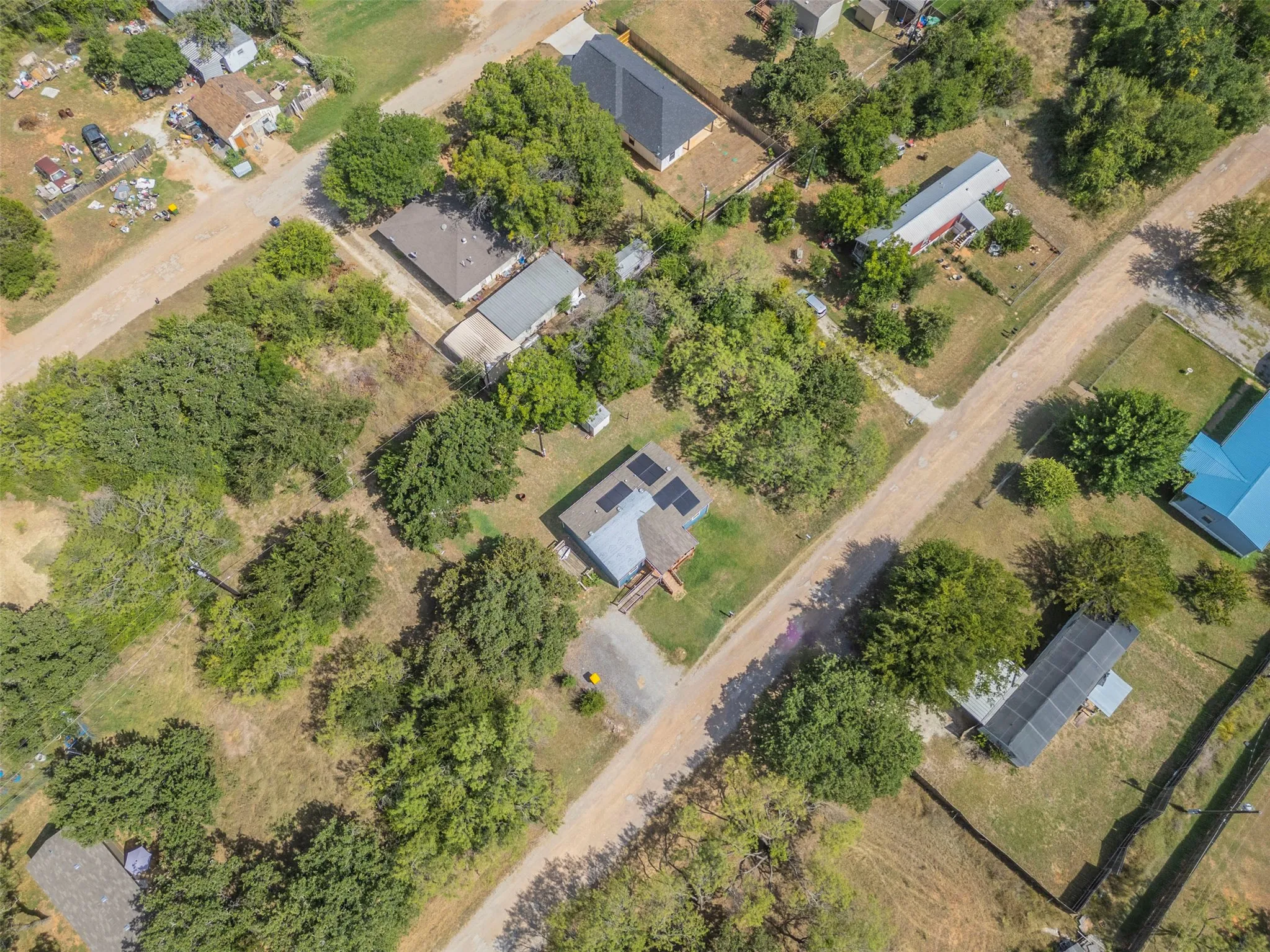 Aerial perspective showcasing a property surrounded by mature trees, featuring a main structure with a metal roof and an adjacent covered structure