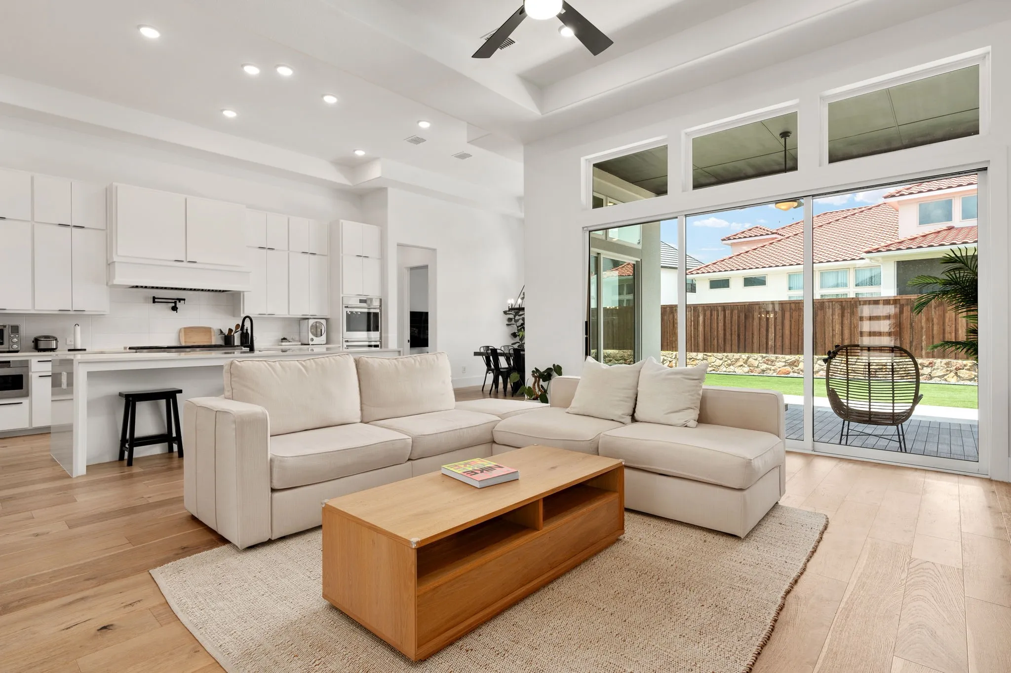 Open-concept living space featuring wood-finish flooring, a contemporary kitchen with white cabinetry, a large sliding glass door with transom windows, and recessed lighting