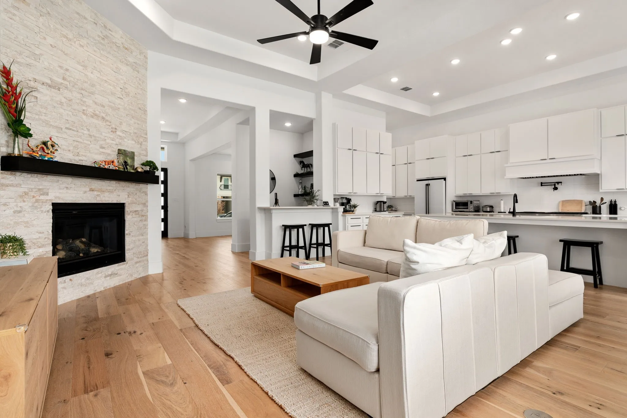 Spacious living area featuring light wood-finish flooring, a stone-clad fireplace with a dark wood mantel, and recessed lighting