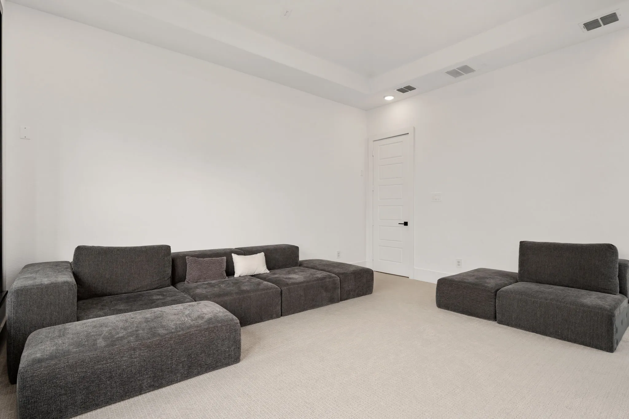 Spacious room featuring neutral carpeting, white walls, a tray ceiling, recessed lighting, and a five-panel interior door with dark hardware