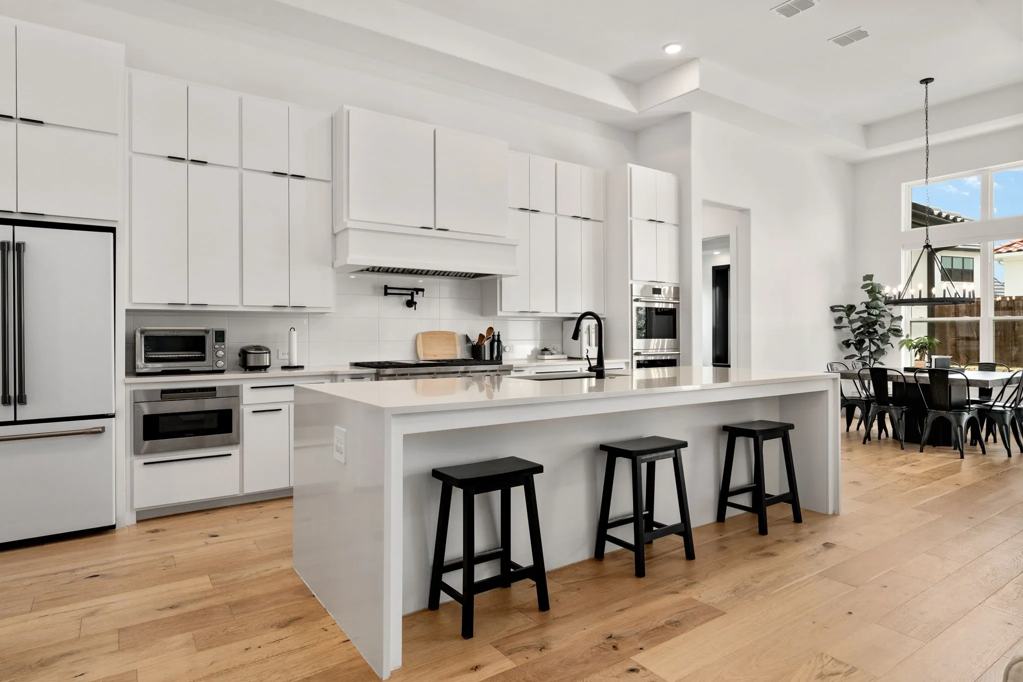 Spacious kitchen featuring an expansive island with a waterfall countertop, integrated stainless steel appliances, abundant white cabinetry, and wood-finish flooring