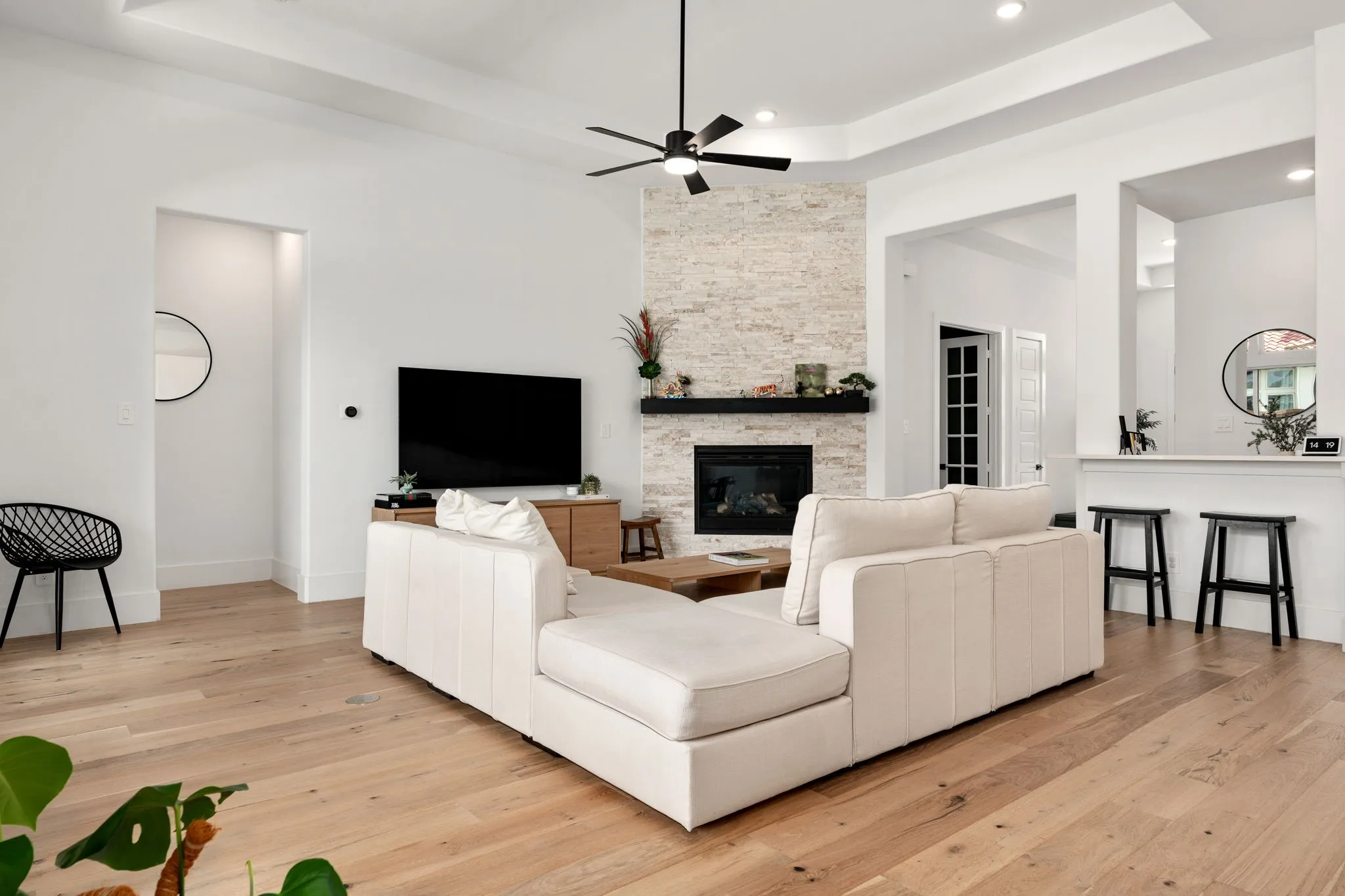 Spacious living area featuring light wood-finish flooring, a stone-clad fireplace with a dark mantel, and recessed lighting