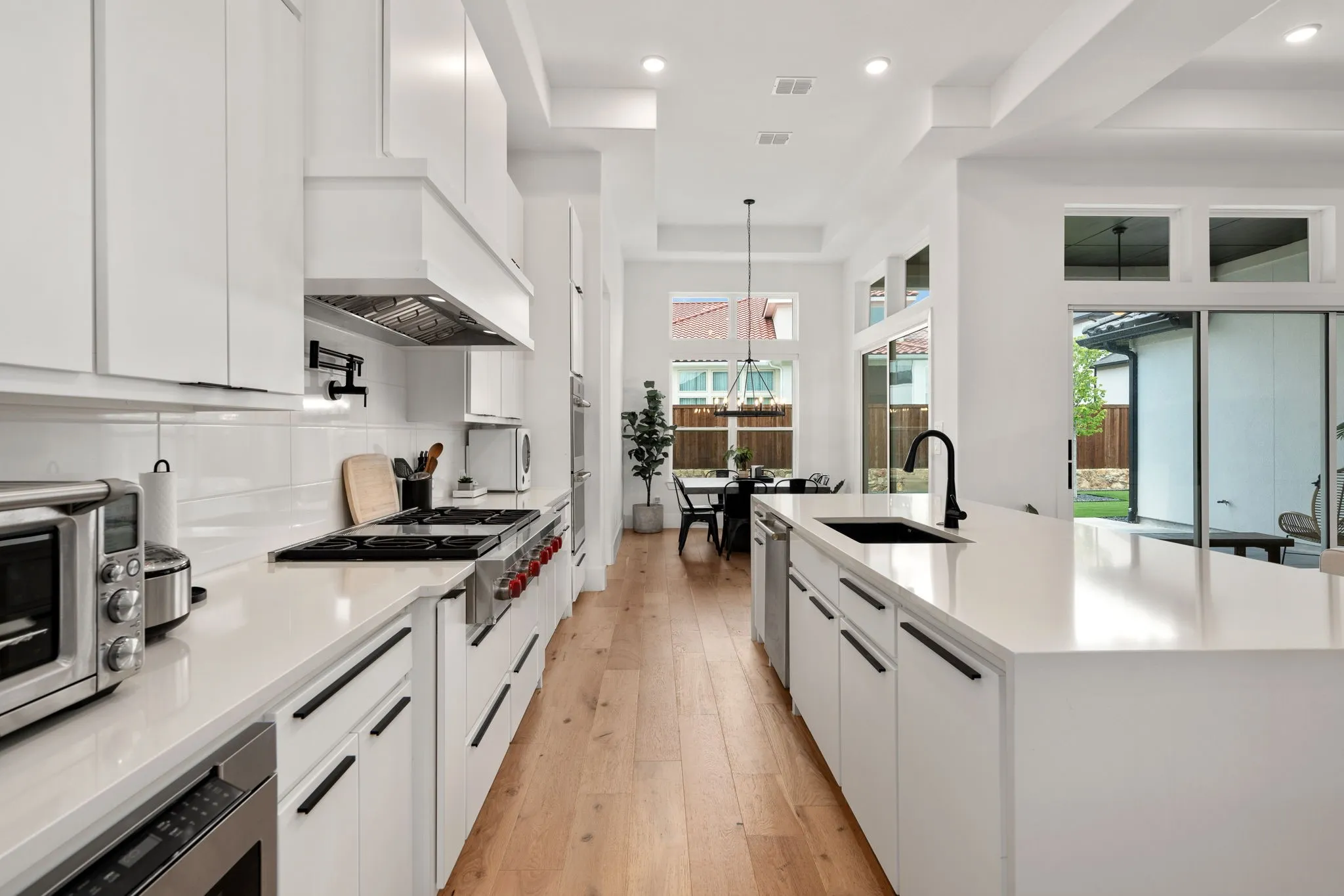 Gourmet kitchen featuring extensive white cabinetry, white countertops, built-in stainless steel appliances, wood-finish flooring, and recessed lighting
