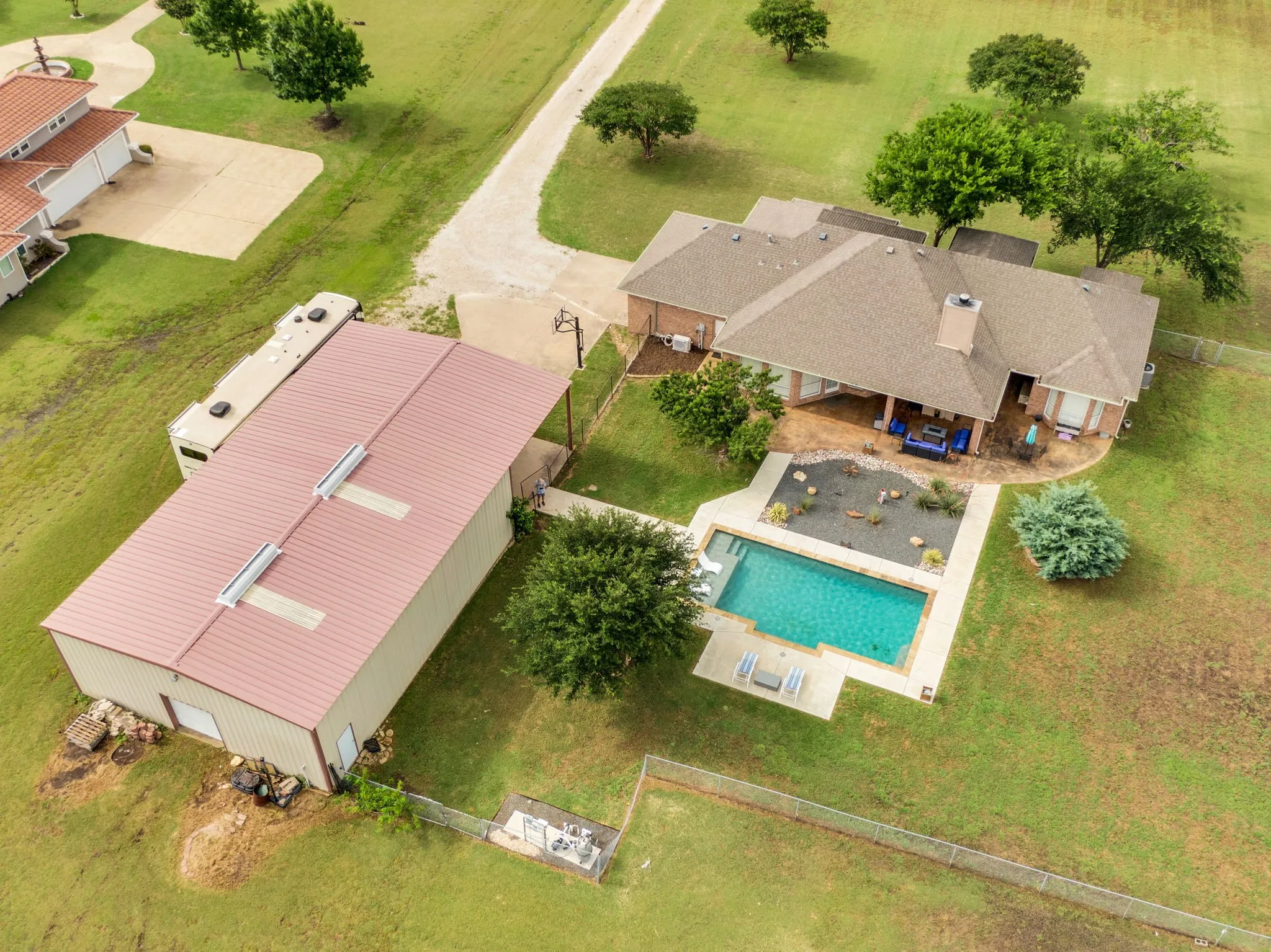 Expansive property featuring a rectangular swimming pool with concrete decking, a covered patio, a detached metal-sided outbuilding with a metal roof, and a gravel driveway