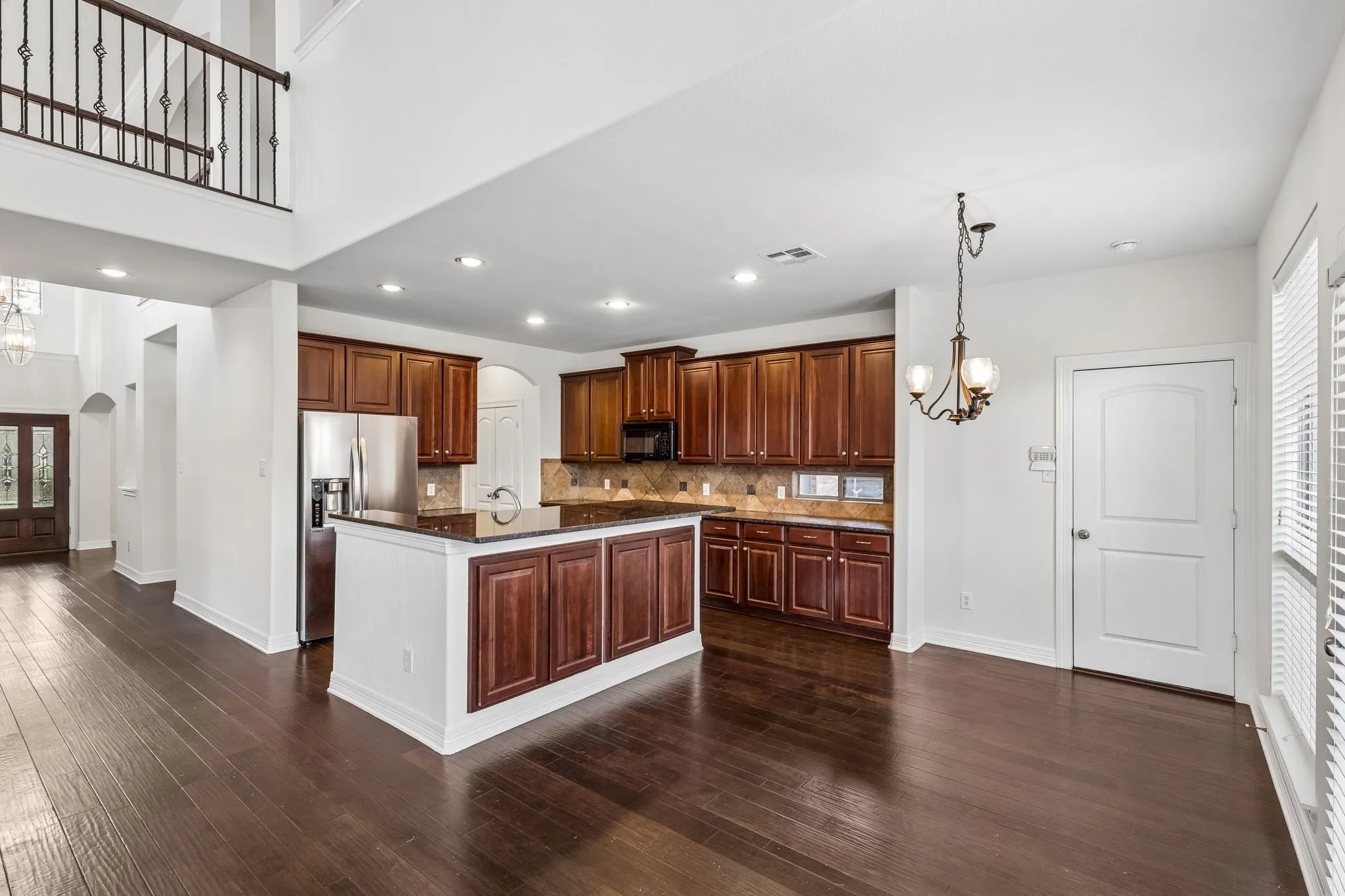 Spacious interior featuring dark wood-finish flooring, a kitchen island with dark cabinetry, stainless steel appliances, and a two-story entry