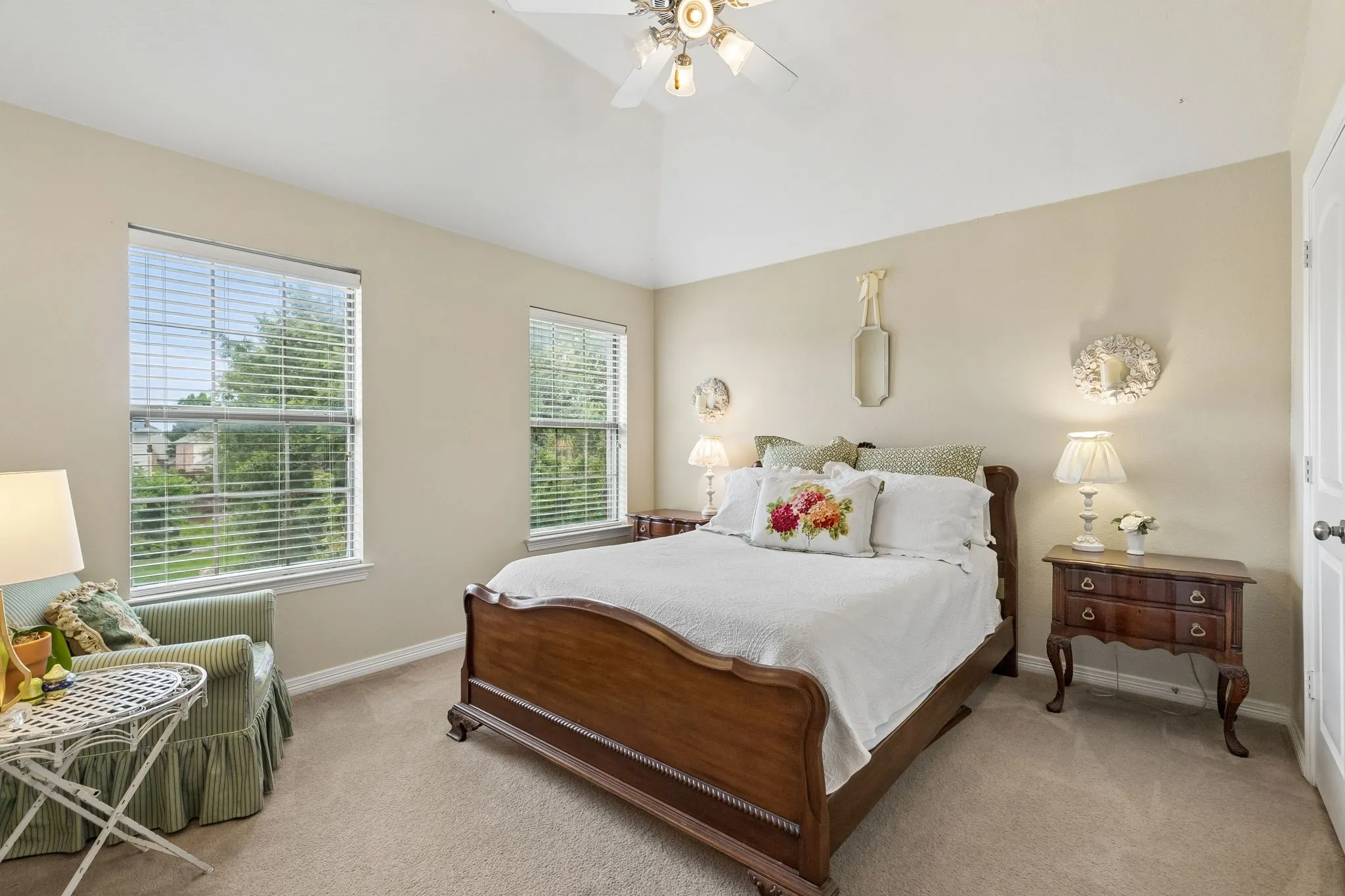 Vaulted ceiling with a ceiling fan, two windows with blinds, neutral carpet flooring, and a white paneled door