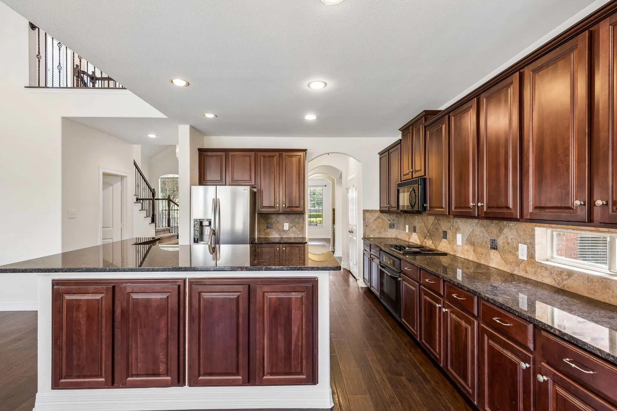 Spacious kitchen featuring rich wood cabinetry, dark stone countertops, stainless steel appliances, a tiled backsplash, and wood-finish flooring