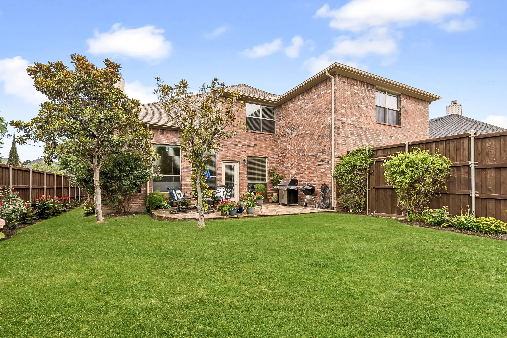 Spacious backyard featuring a large green lawn, mature trees, and a flagstone patio