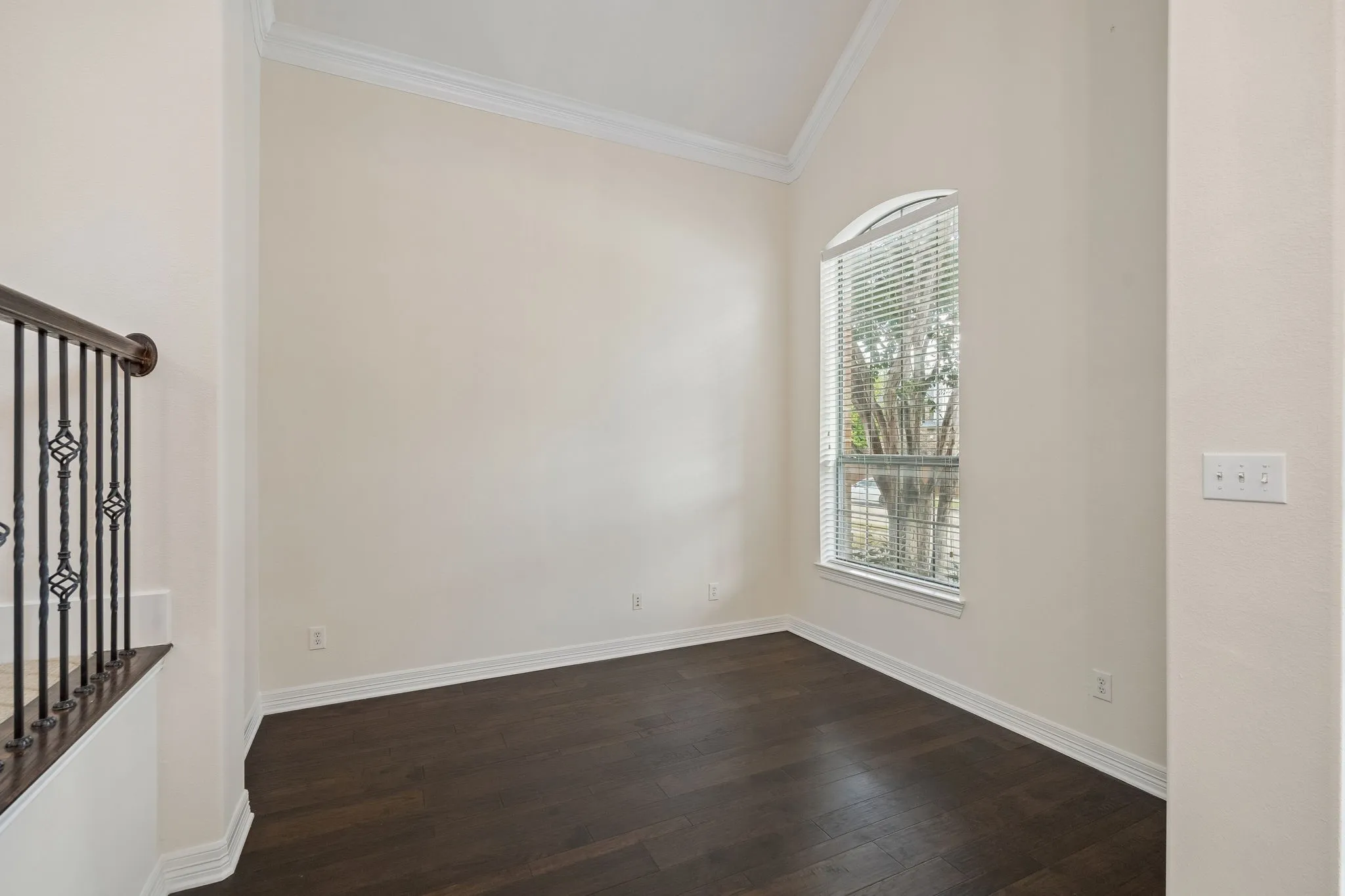 Arched window, high vaulted ceilings, crown molding, dark wood-finish flooring, and wrought iron balusters