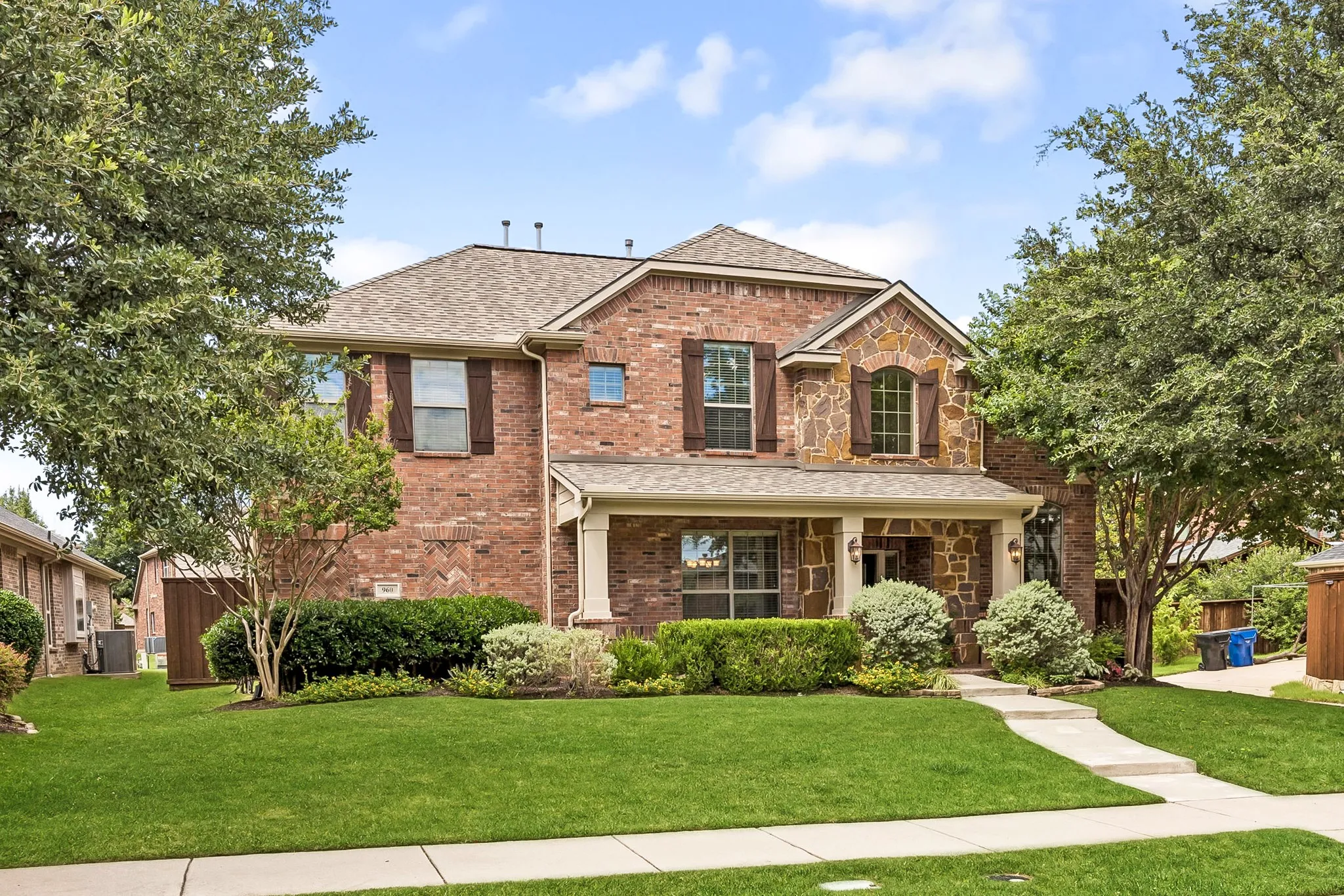 Two-story brick and stone exterior featuring a covered front porch with columns, a gabled roof, and dark shutters