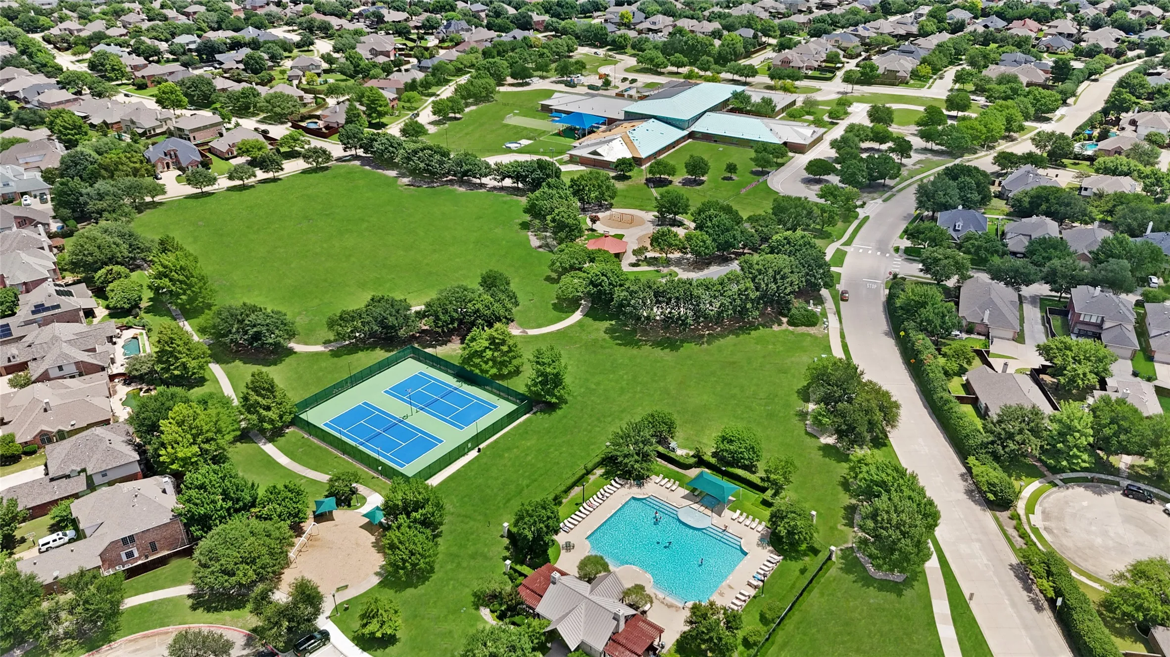 Aerial perspective showcasing a community park with expansive green space, two tennis courts, and a swimming pool area
