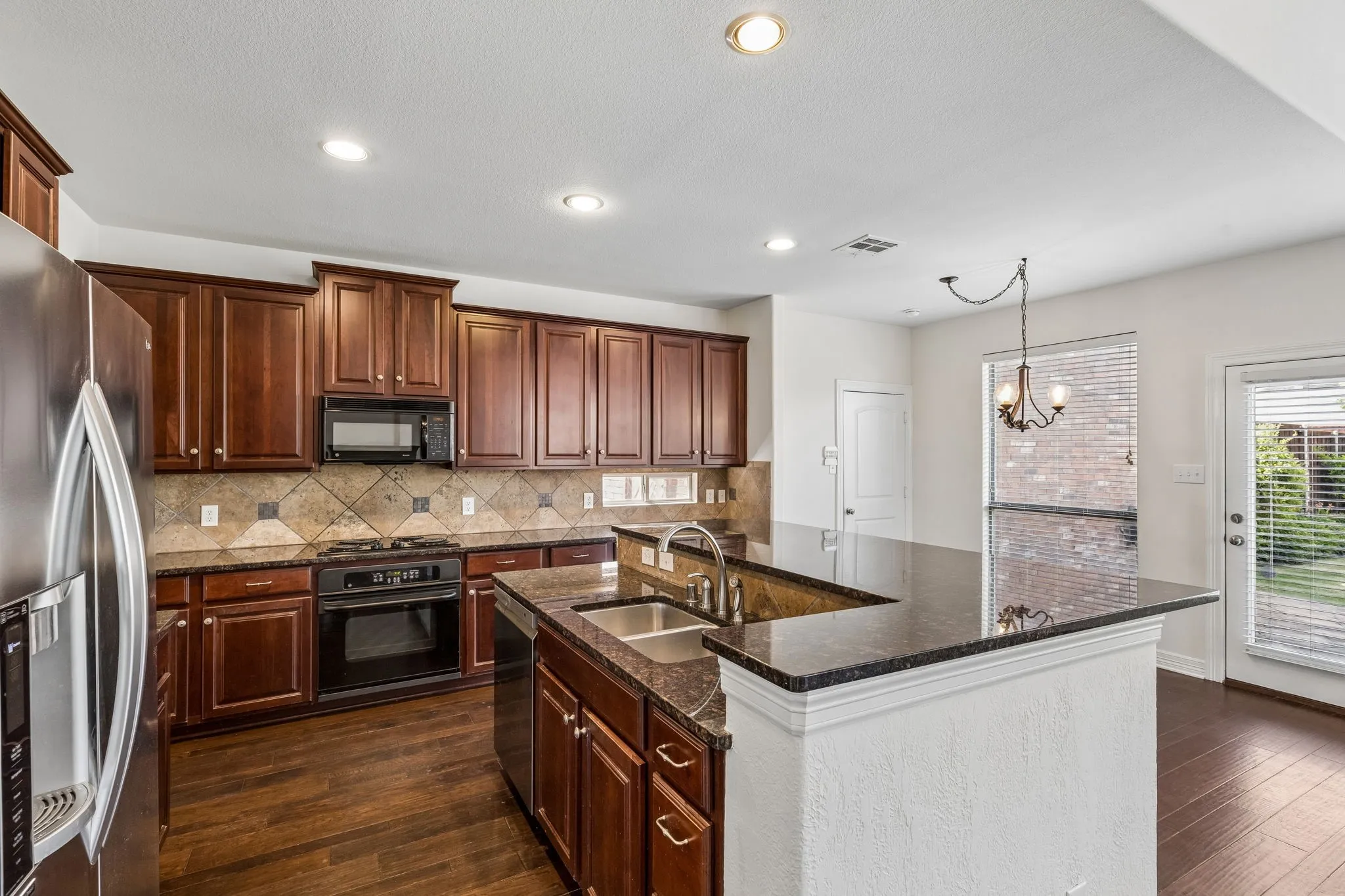Kitchen featuring dark wood cabinetry, stainless steel refrigerator, black range, and granite countertops