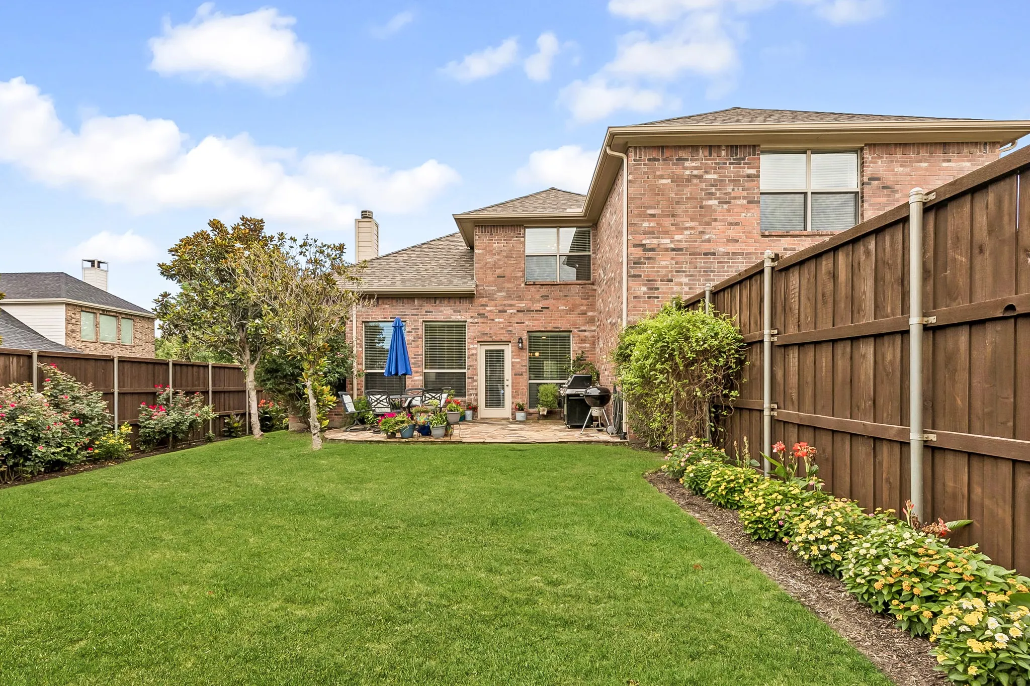 Spacious backyard featuring a substantial lawn, a stone patio, and mature landscaping
