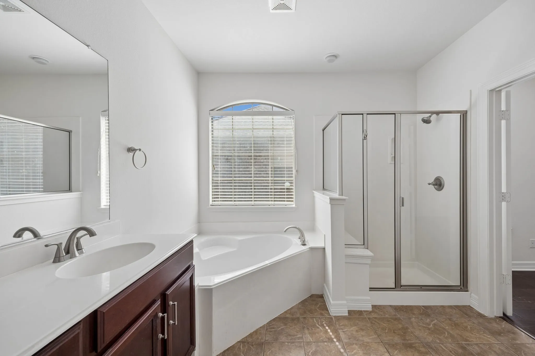 Corner soaking tub, separate glass-enclosed shower, dual vanity with undermount sinks, and an arched window