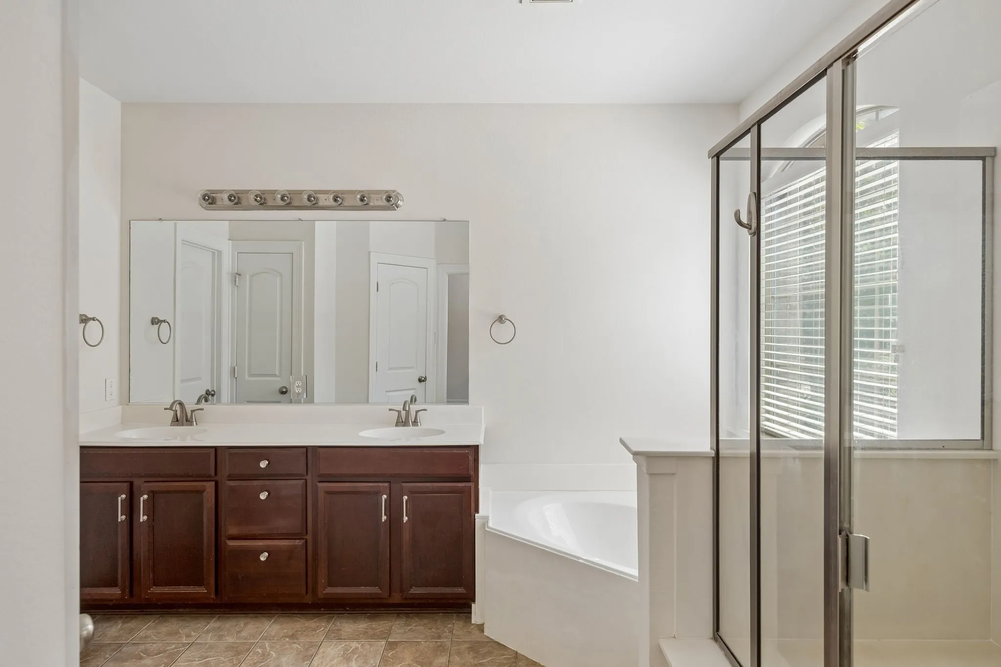 Dual vanity with dark wood-finish cabinetry, built-in soaking tub, and glass-enclosed shower