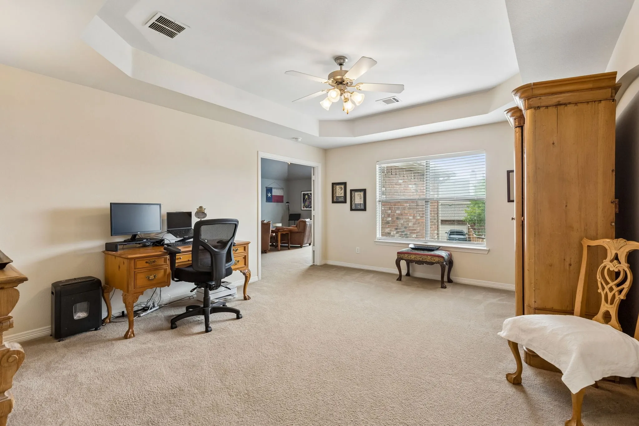 Recessed ceiling with ceiling fan, neutral carpeting, window with blinds, and doorway to an additional room