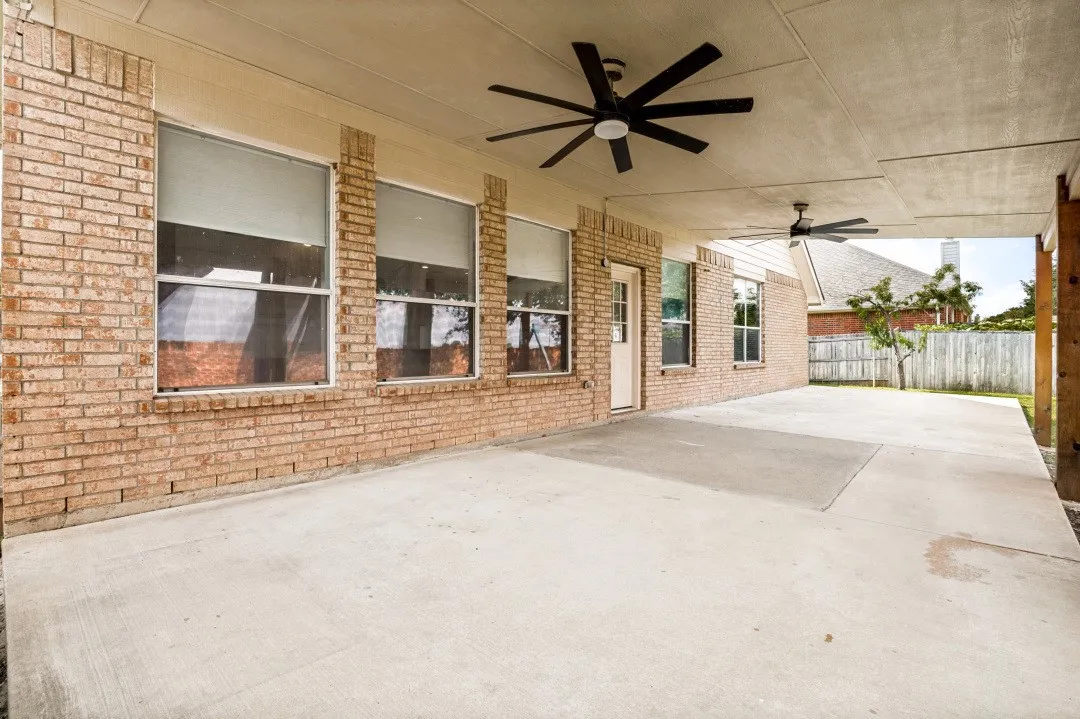 Expansive covered patio featuring a concrete surface, brick exterior wall, multiple windows, and two ceiling fans