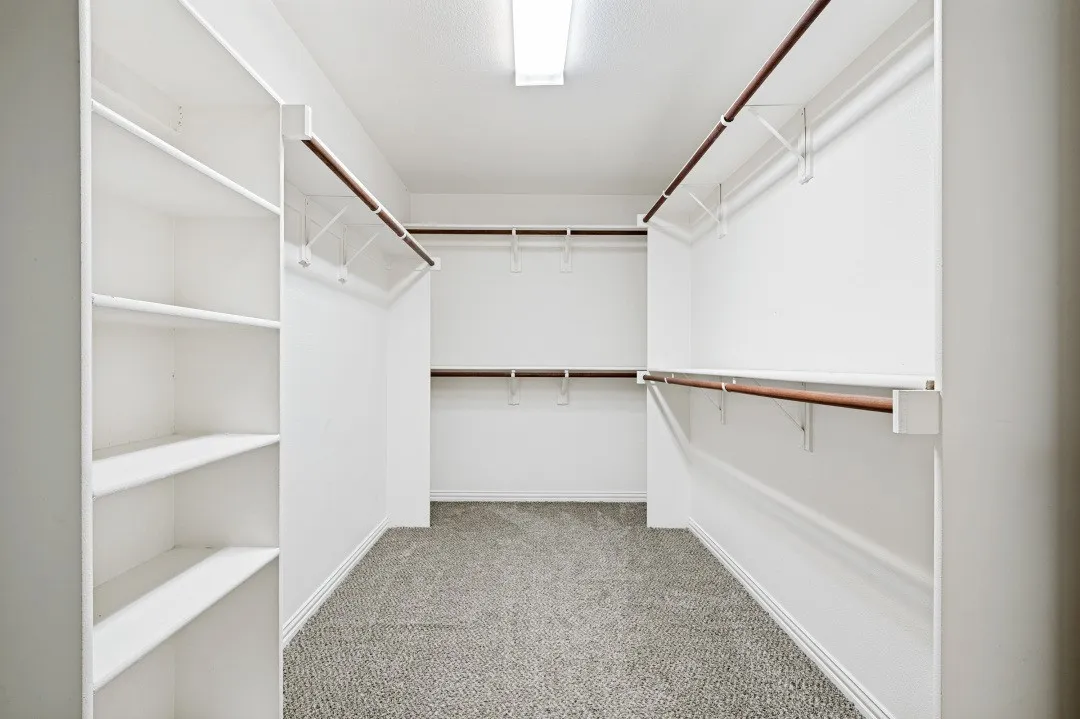Walk-in closet featuring built-in shelving, multiple hanging rods, and neutral-toned carpeting