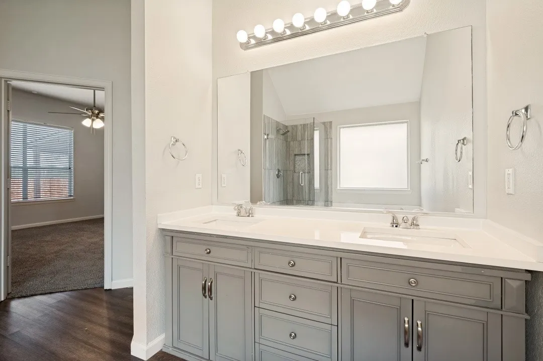 Dual vanity with light gray cabinetry, integrated sinks, chrome fixtures, and a full-width mirror