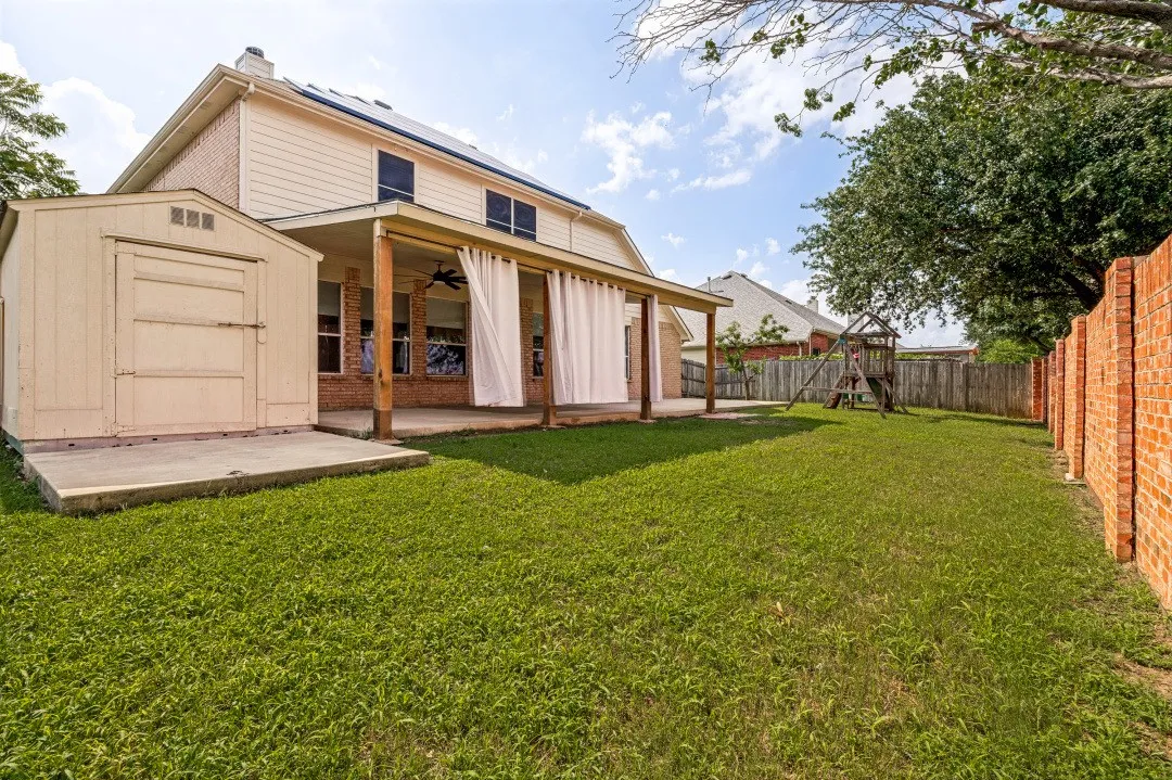 Spacious backyard with a covered patio, brick exterior, and a detached storage shed
