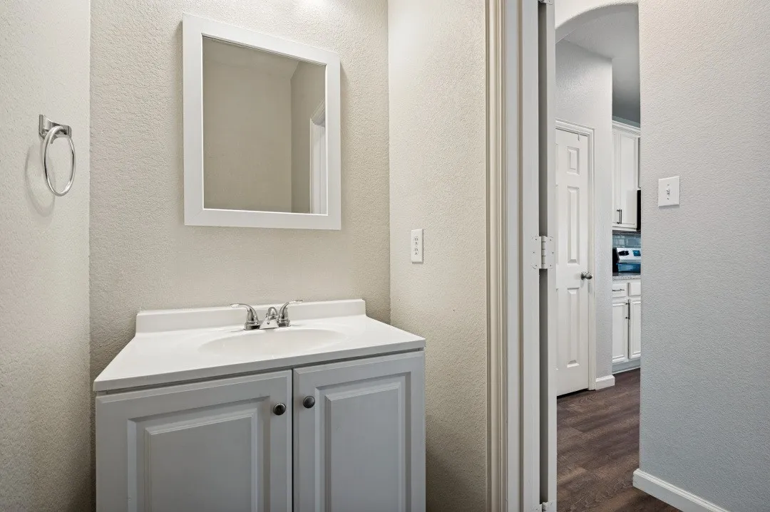 White vanity with an integrated sink and chrome faucet, framed mirror, and chrome towel ring