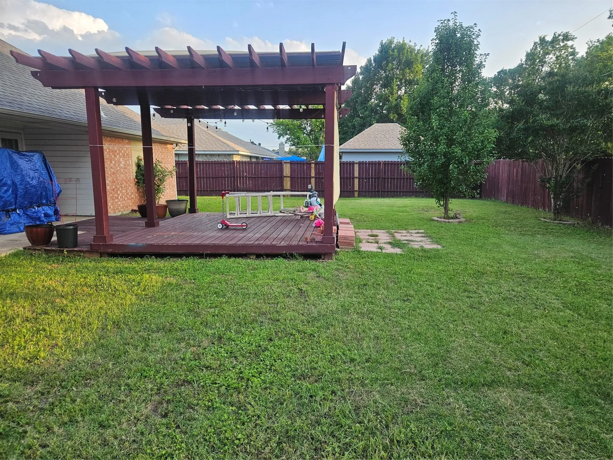Expansive backyard featuring a stained wood pergola with string lighting, a large wood-finish deck, and a mature tree