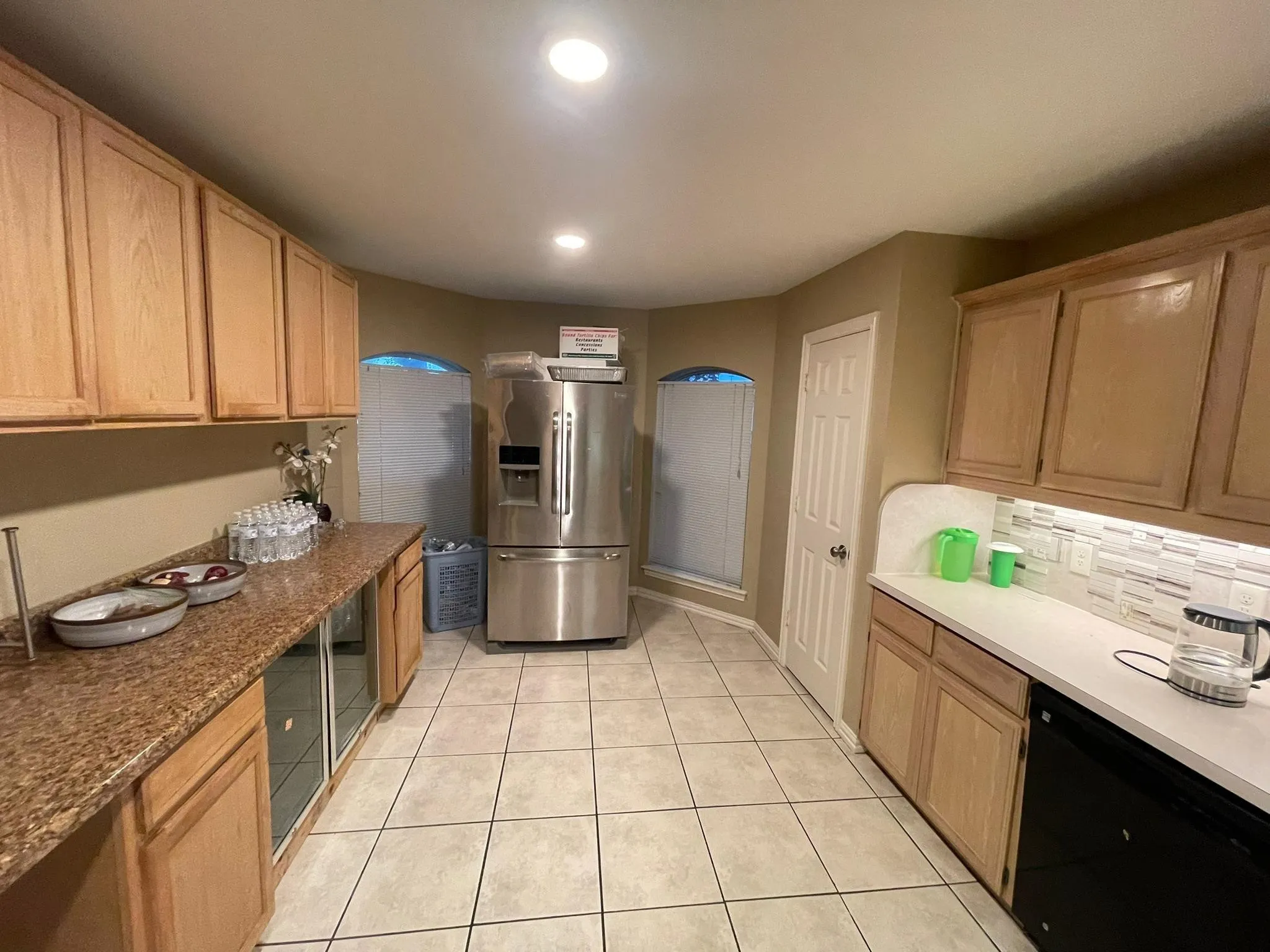 Kitchen featuring light wood cabinetry, a stainless steel refrigerator, white tile flooring, recessed ceiling lights, and arched windows