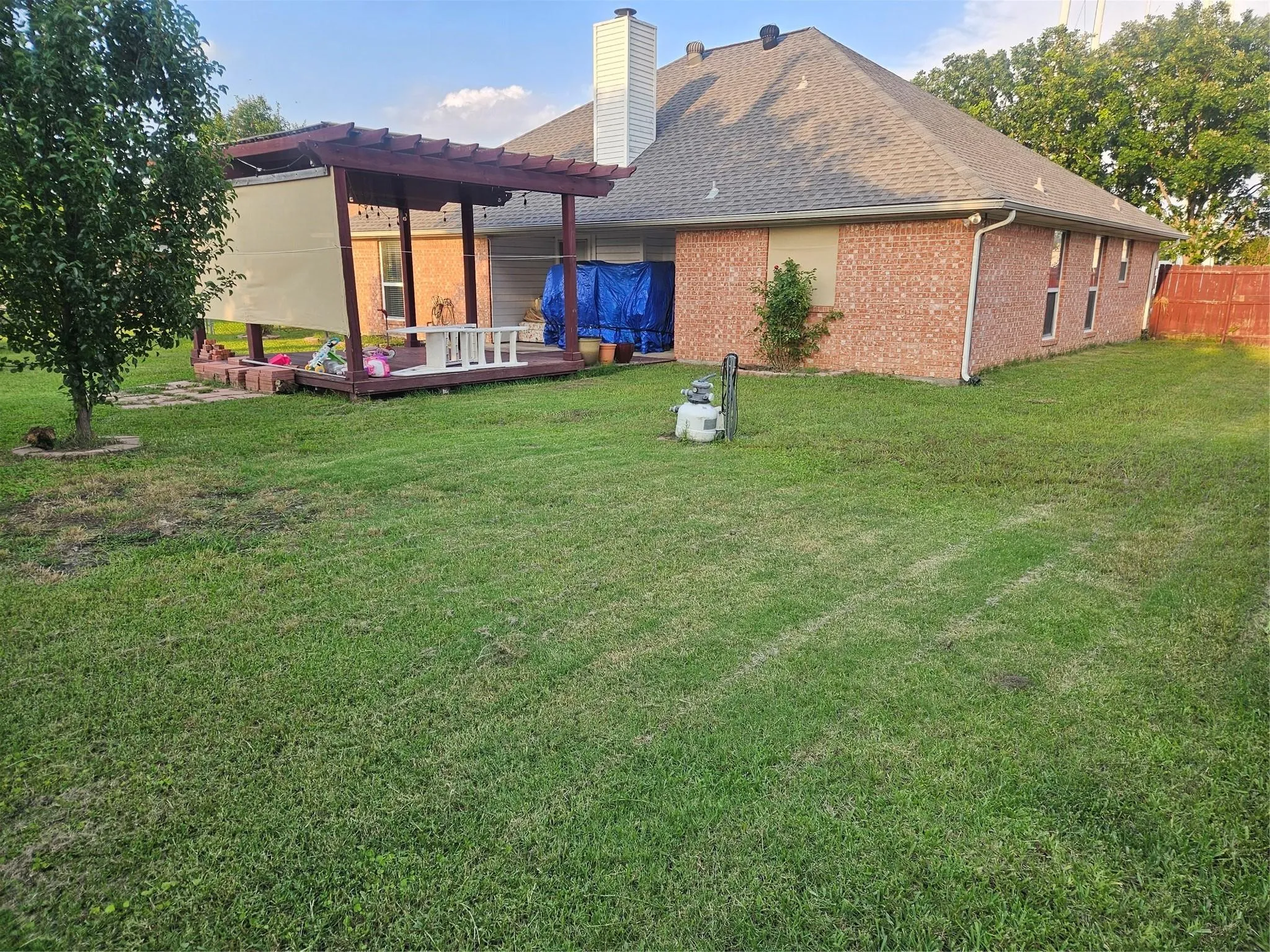 Spacious backyard featuring a wood pergola with shade screens, a raised wooden deck area, and a large expanse of green lawn