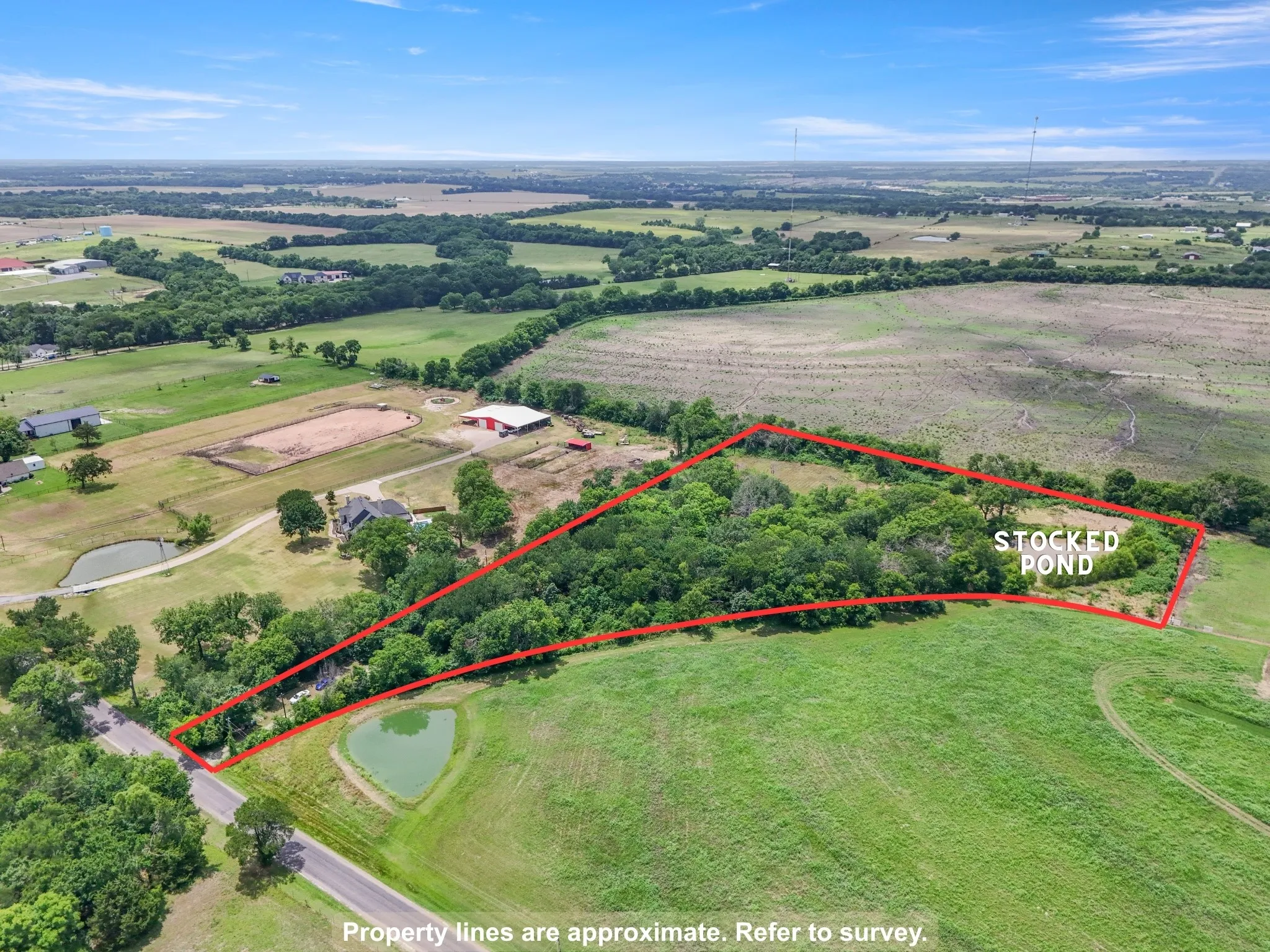 Wide aerial view highlighting the wooded acreage, pond area, and surrounding rural setting.