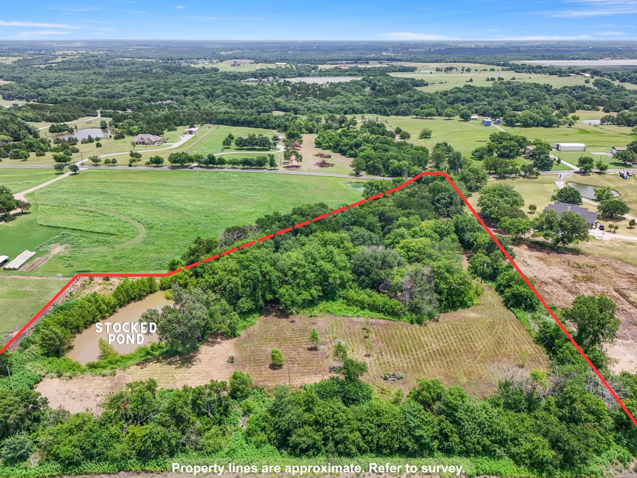 Aerial perspective showing the wooded interior, open clearing, pond, and surrounding acreage.