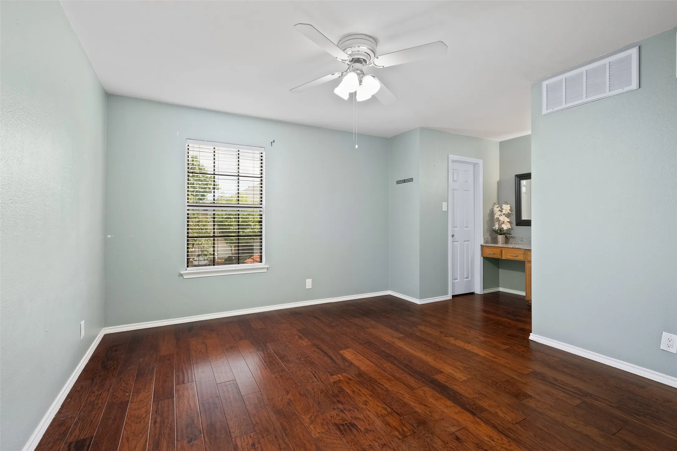 Well-proportioned secondary bedroom with hardwood floors, a ceiling fan, natural light, closet, and a built-in vanity area with granite countertop — a versatile space for guest or office use.