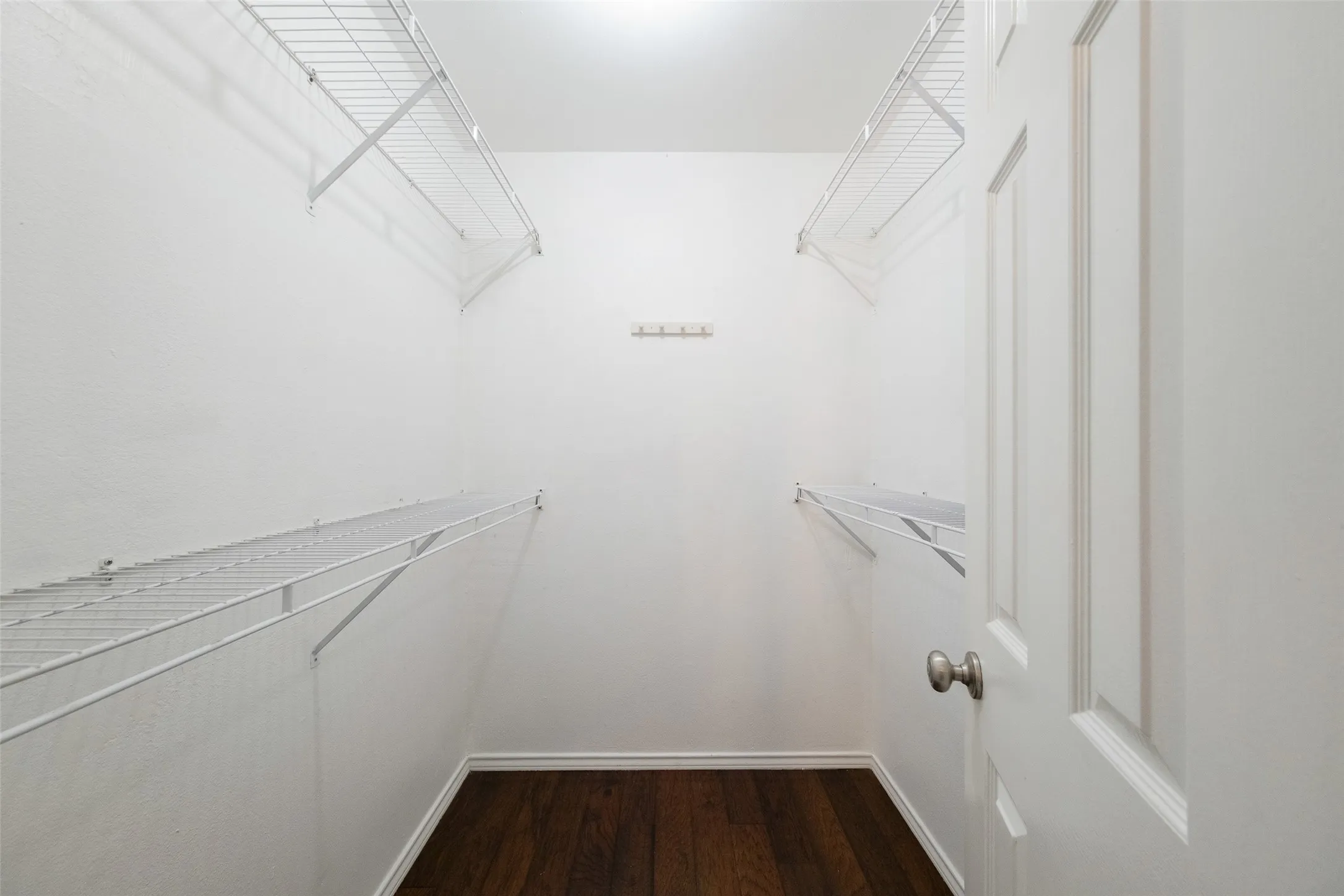 Generously sized walk-in closet off the primary suite with dual hanging rods, upper shelving on both sides, and hardwood floors — plenty of room to customize to your storage needs.