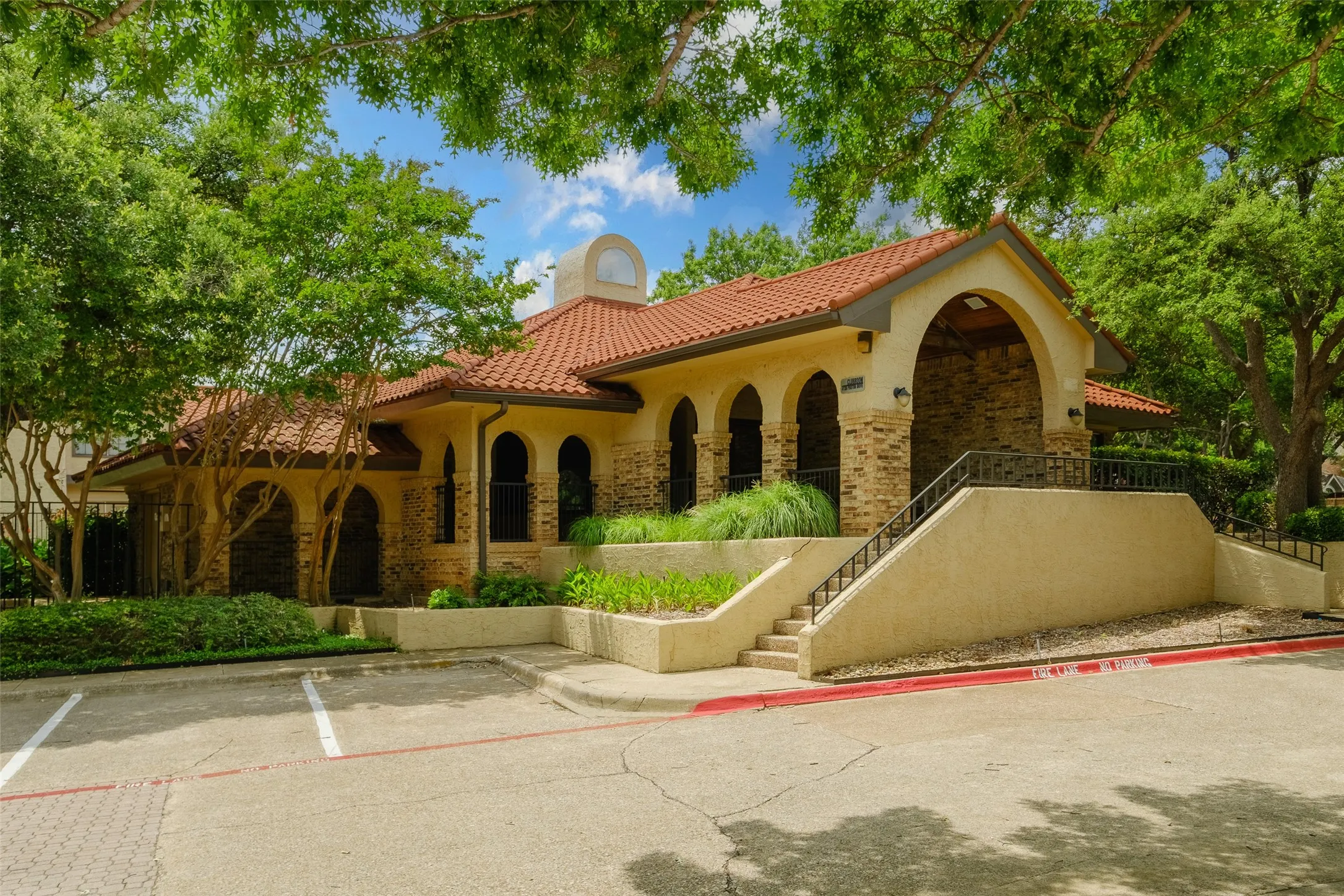 La Mirada's Spanish-style clubhouse featuring a clay tile roof, arched brick colonnade, and lush surrounding landscaping — available for residents and a testament to the community's well-maintained character.