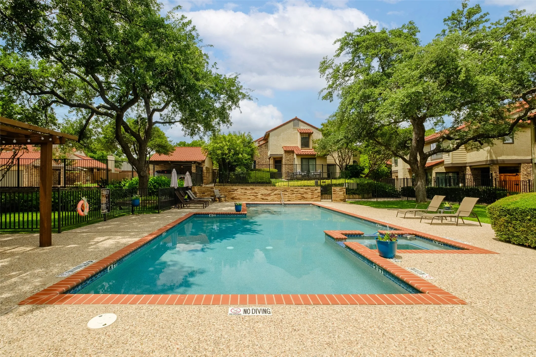 Resort-style community pool with brick coping, spa, lounge chairs, pergola, and mature live oak canopy — a peaceful escape steps from your front door.