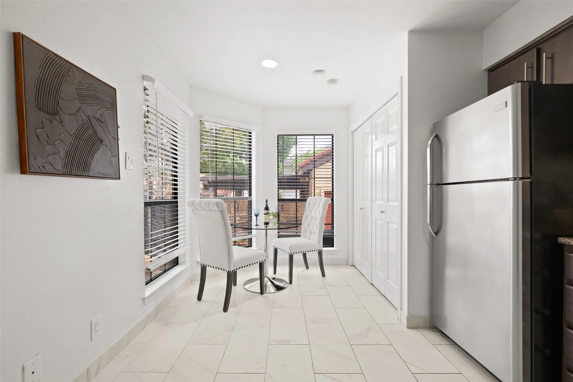 Bright breakfast nook with large windows, marble-look tile flooring, and a cozy two-seat café table — the perfect morning coffee spot with natural light on all sides.