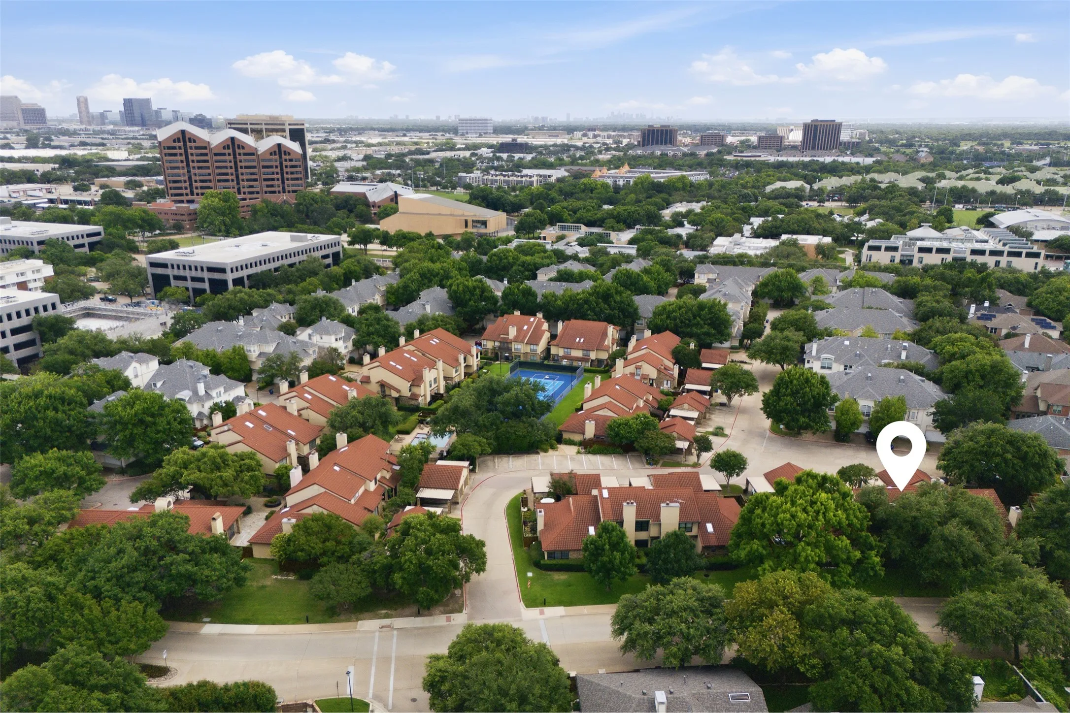 Wide aerial perspective of La Mirada's full footprint surrounded by mature tree canopy, with the Addison skyline in the background — highlighting the rare combination of a quiet, green neighborhood setting with immediate urban access.