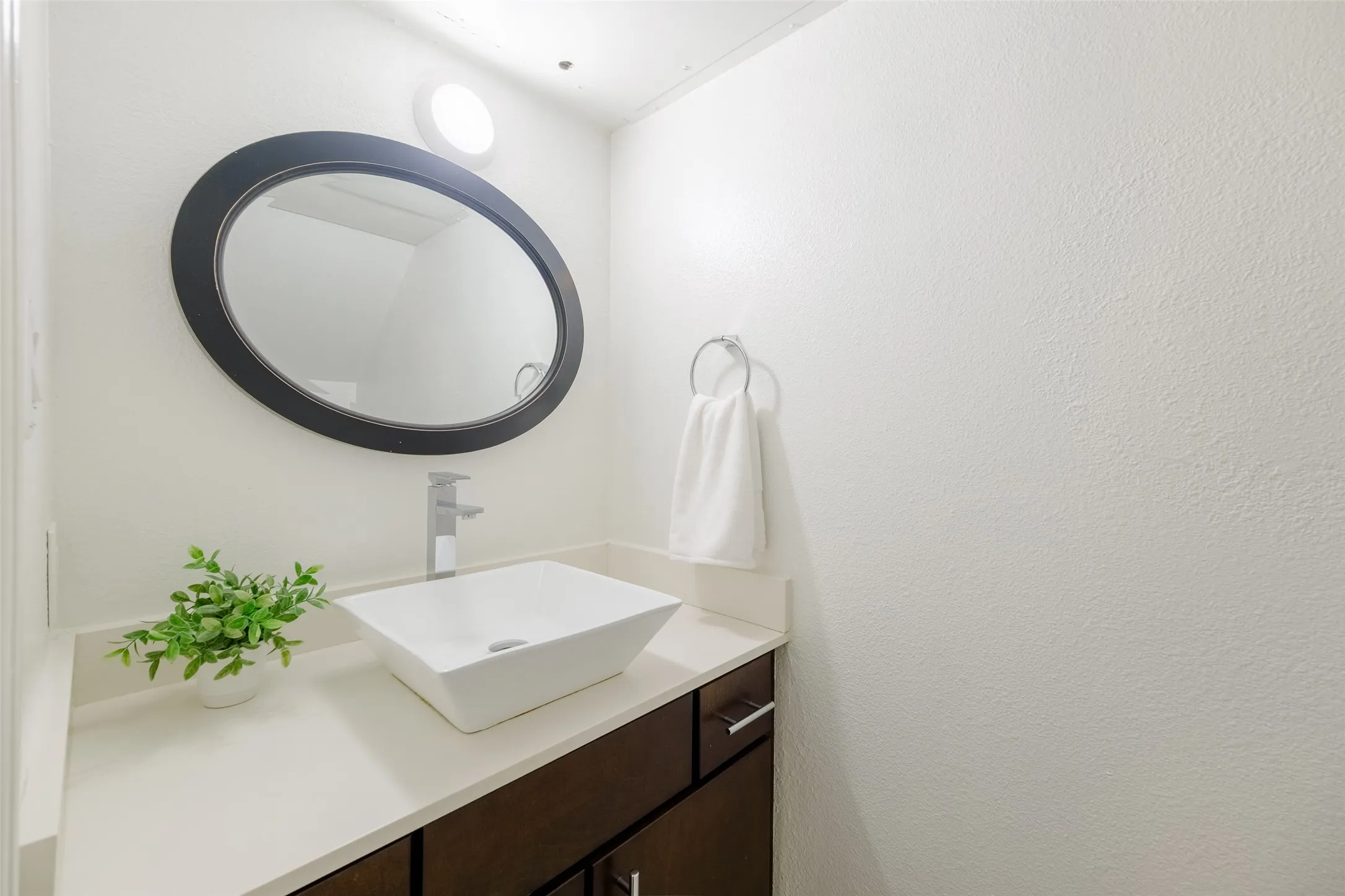 Updated half-bath with a white vessel sink, sleek chrome faucet, quartz countertop, and dark wood cabinetry — a modern, clean finish for guests.